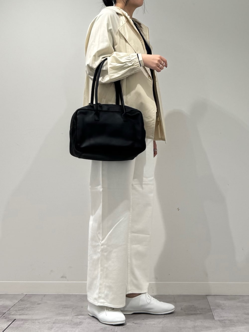 ブラック系のボストンバッグ、ホワイト系のトレンチコート、ホワイト系のデニムパンツを着用したレディースの冬コーディネートの2枚目の写真