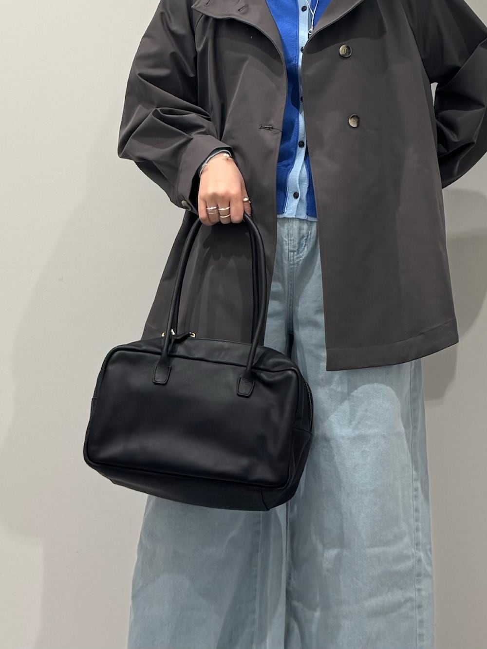 グレー系のトレンチコート、ブラック系のボストンバッグ、ブルー系のデニムパンツを着用したレディースの冬コーディネートの8枚目の写真