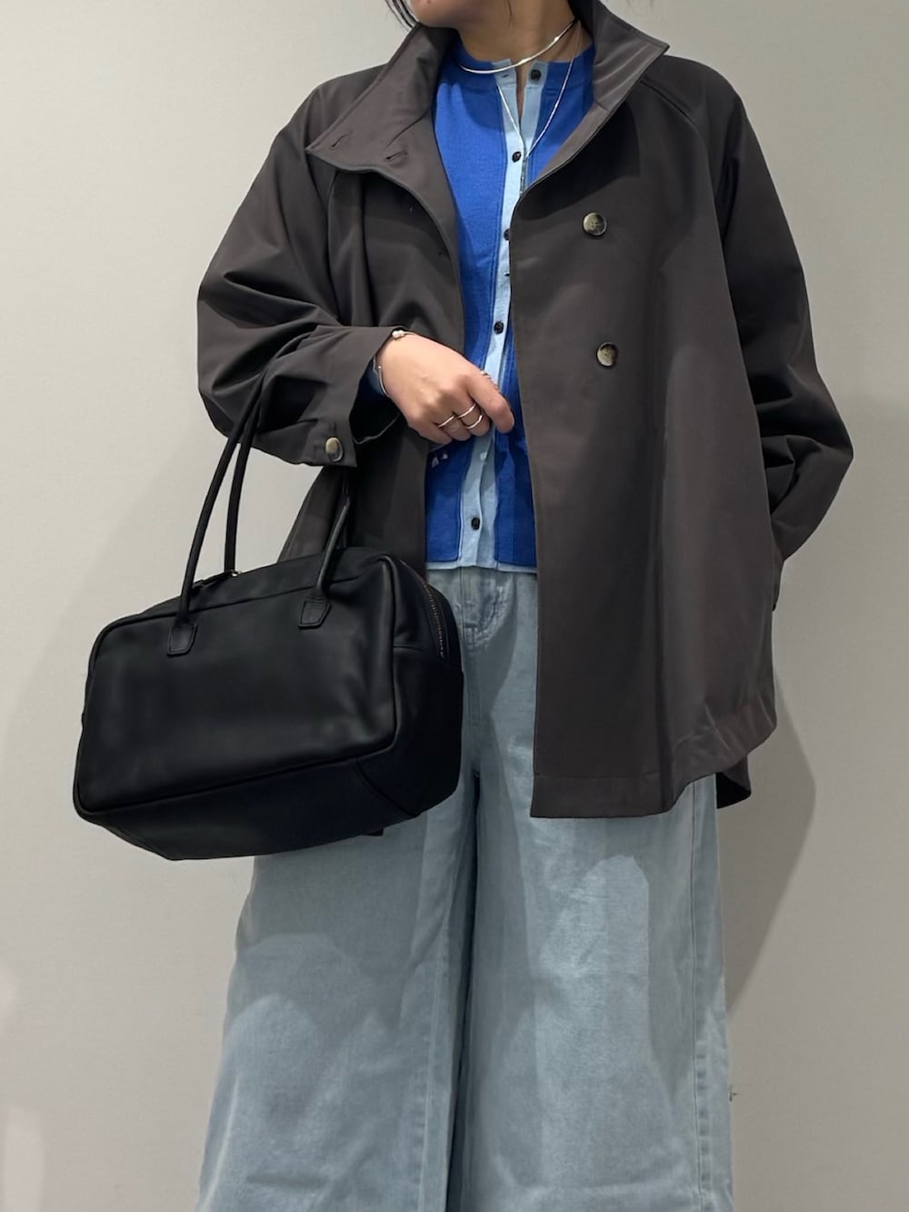 グレー系のトレンチコート、ブラック系のボストンバッグ、ブルー系のデニムパンツを着用したレディースの冬コーディネートの7枚目の写真