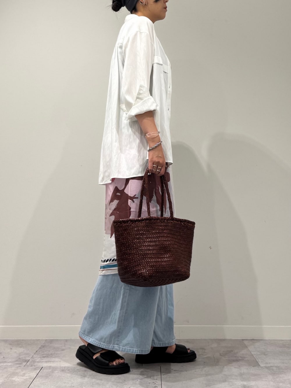 ブラウン系のトートバッグ、ブルー系のデニムパンツ、ブラック系のサンダルを着用したレディースの秋コーディネートの2枚目の写真