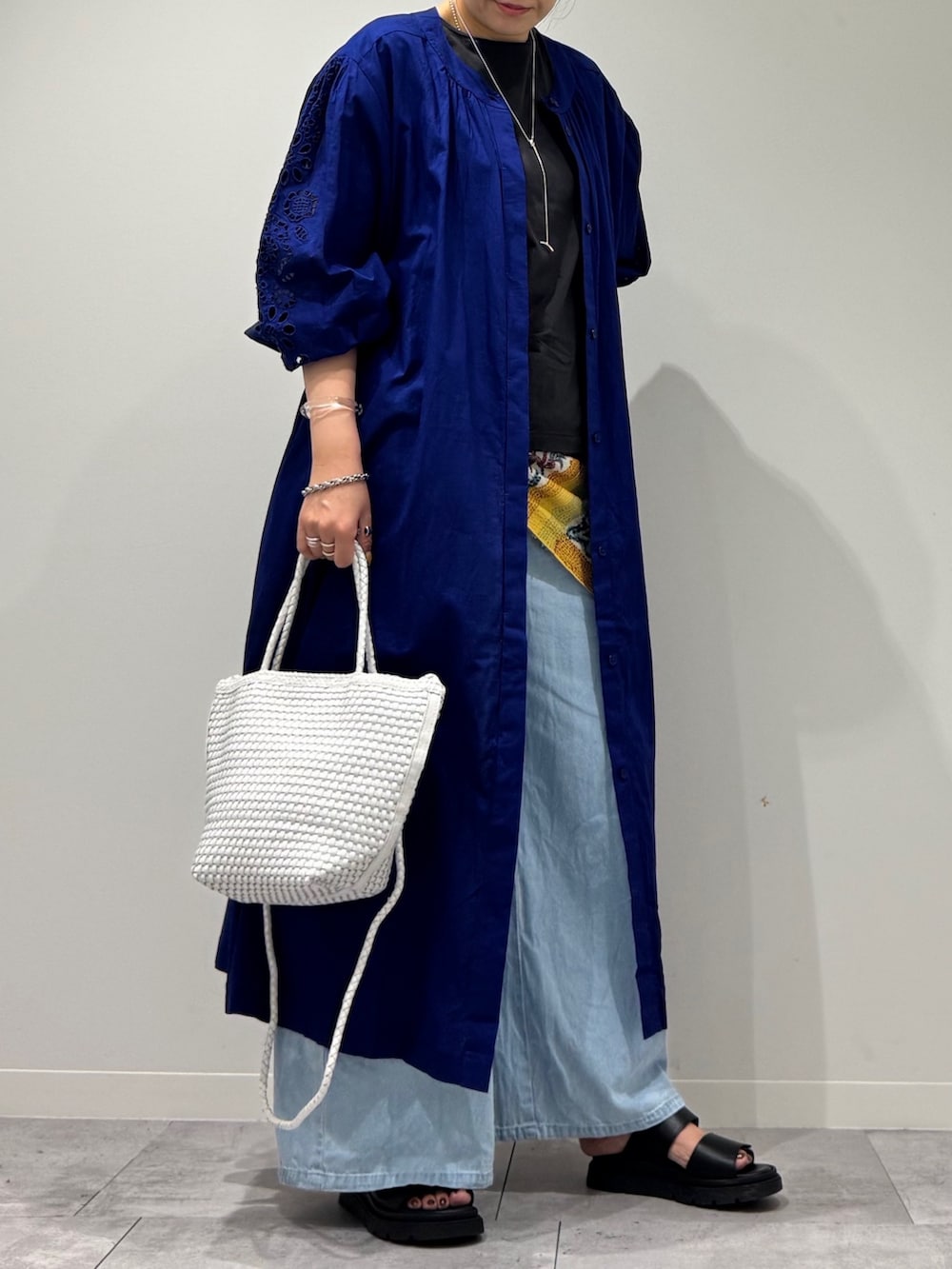 ホワイト系のトートバッグ、ブルー系のデニムパンツ、ブラック系のサンダルを着用したレディースの秋コーディネートの2枚目の写真