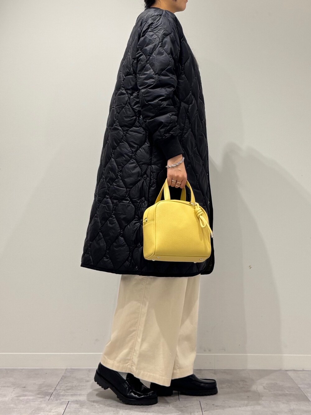 イエロー系のボストンバッグ、ブラウン系のベスト、ホワイト系のその他パンツを着用したレディースの秋コーディネートの2枚目の写真