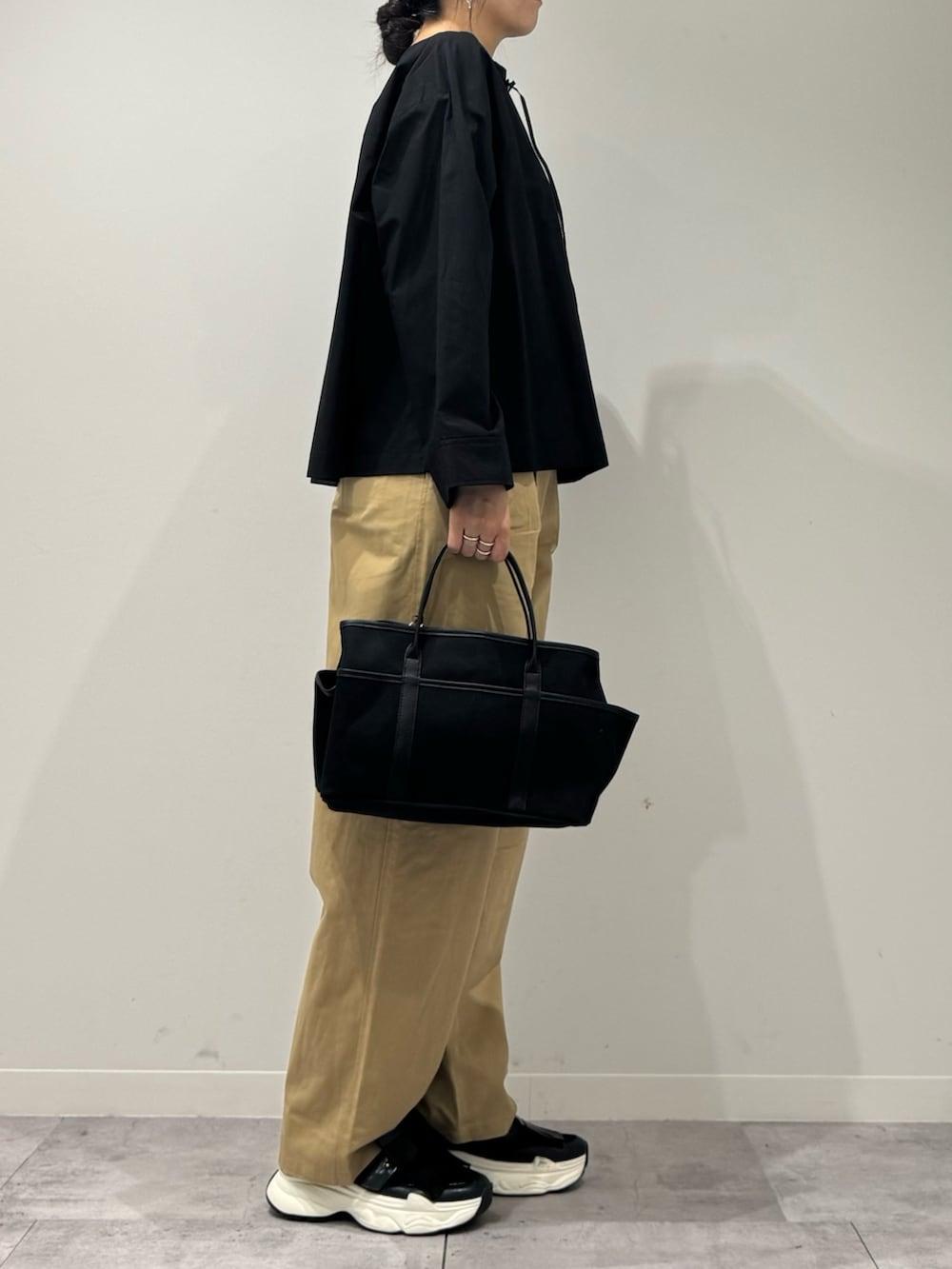 ブラック系のスニーカー、ベージュ系のチノパンツ、ブラック系のシャツ/ブラウスを着用したレディースの秋コーディネートの2枚目の写真