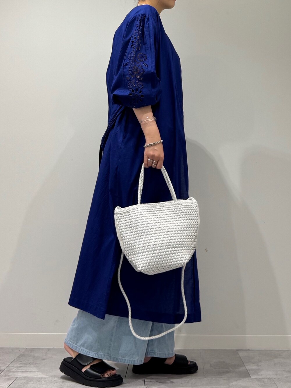 ホワイト系のトートバッグ、ブルー系のデニムパンツ、ブラック系のサンダルを着用したレディースの秋コーディネートの3枚目の写真