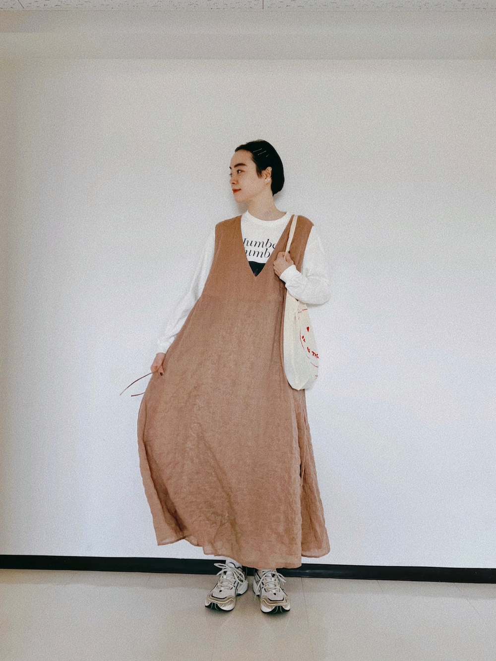 オレンジ系のワンピース、ホワイト系のTシャツ/カットソー、ベージュ系のスニーカーを着用したレディースの春コーディネートの2枚目の写真