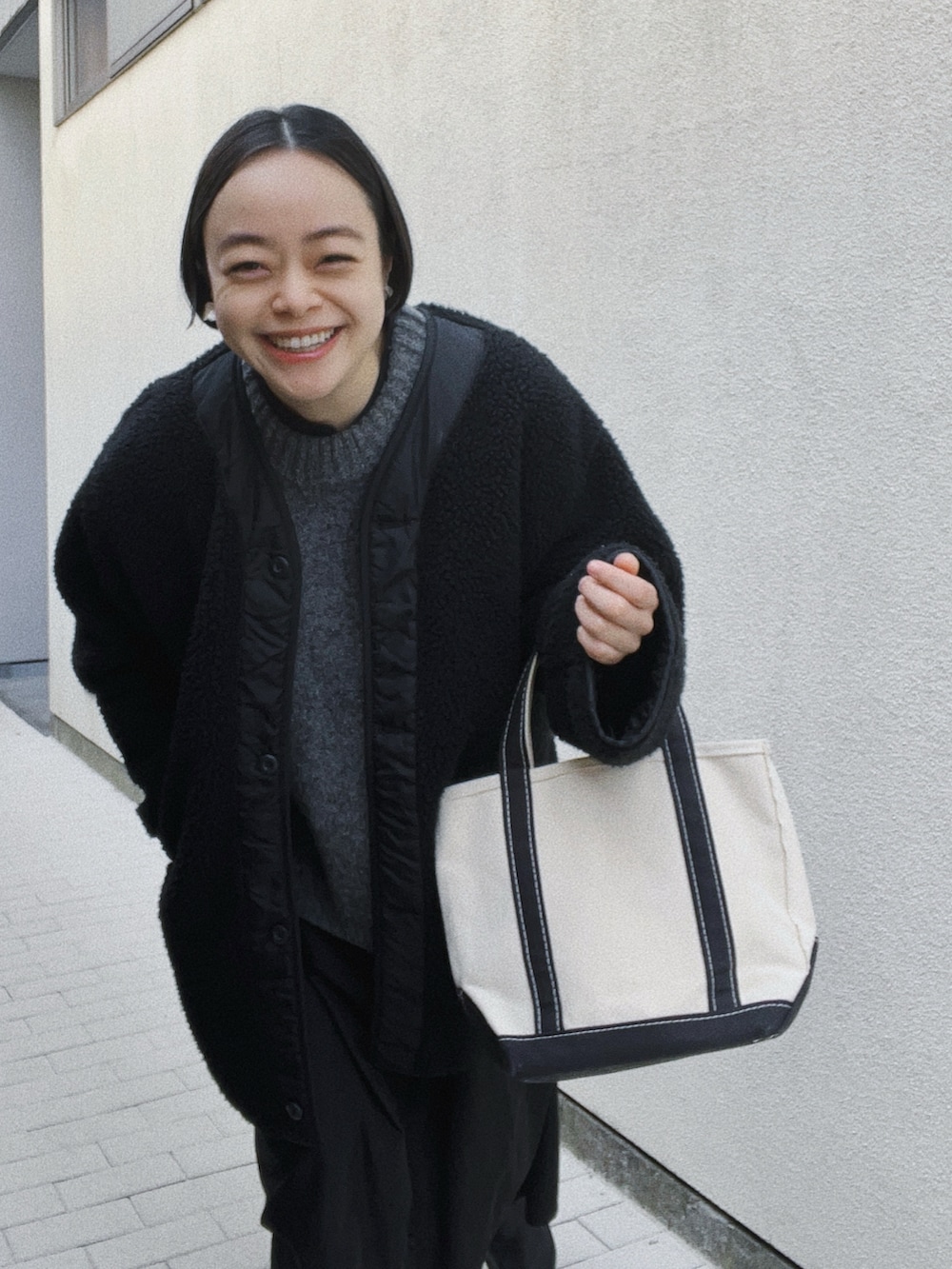 ブラック系のトートバッグ、ブラック系のノーカラージャケット、グレー系のベストを着用したレディースの冬コーディネートの2枚目の写真