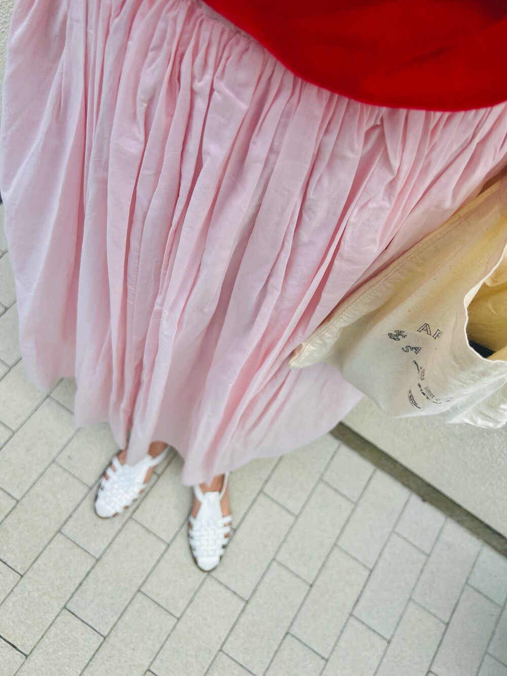 レッド系のTシャツ/カットソー、ピンク系のスカート、ホワイト系のサンダルを着用したレディースの夏コーディネートの2枚目の写真