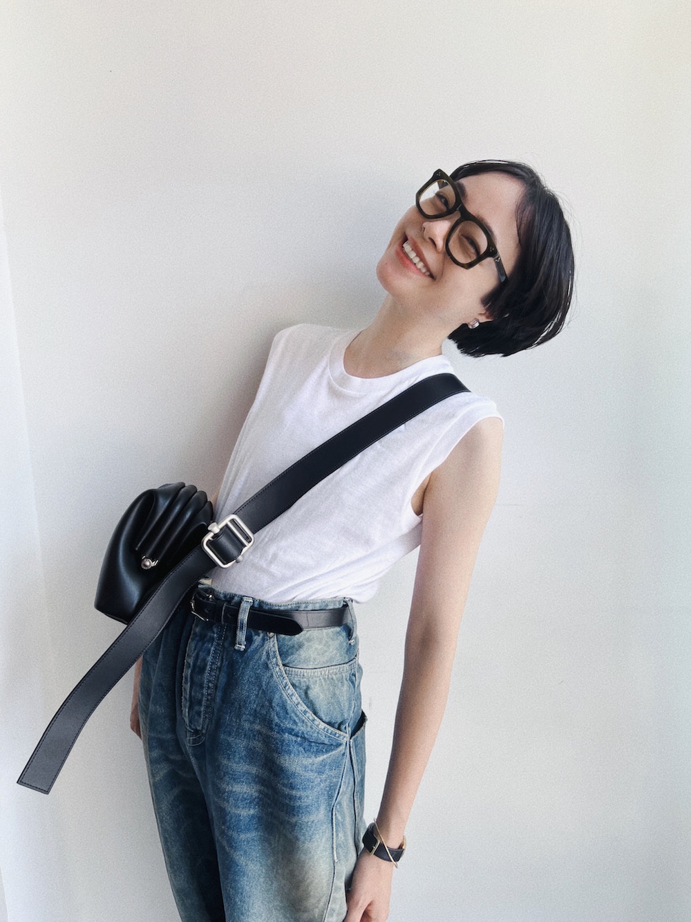 ブラック系のバッグ、ブルー系のデニムパンツ、シルバー系のイヤリングを着用したレディースの夏コーディネートの2枚目の写真