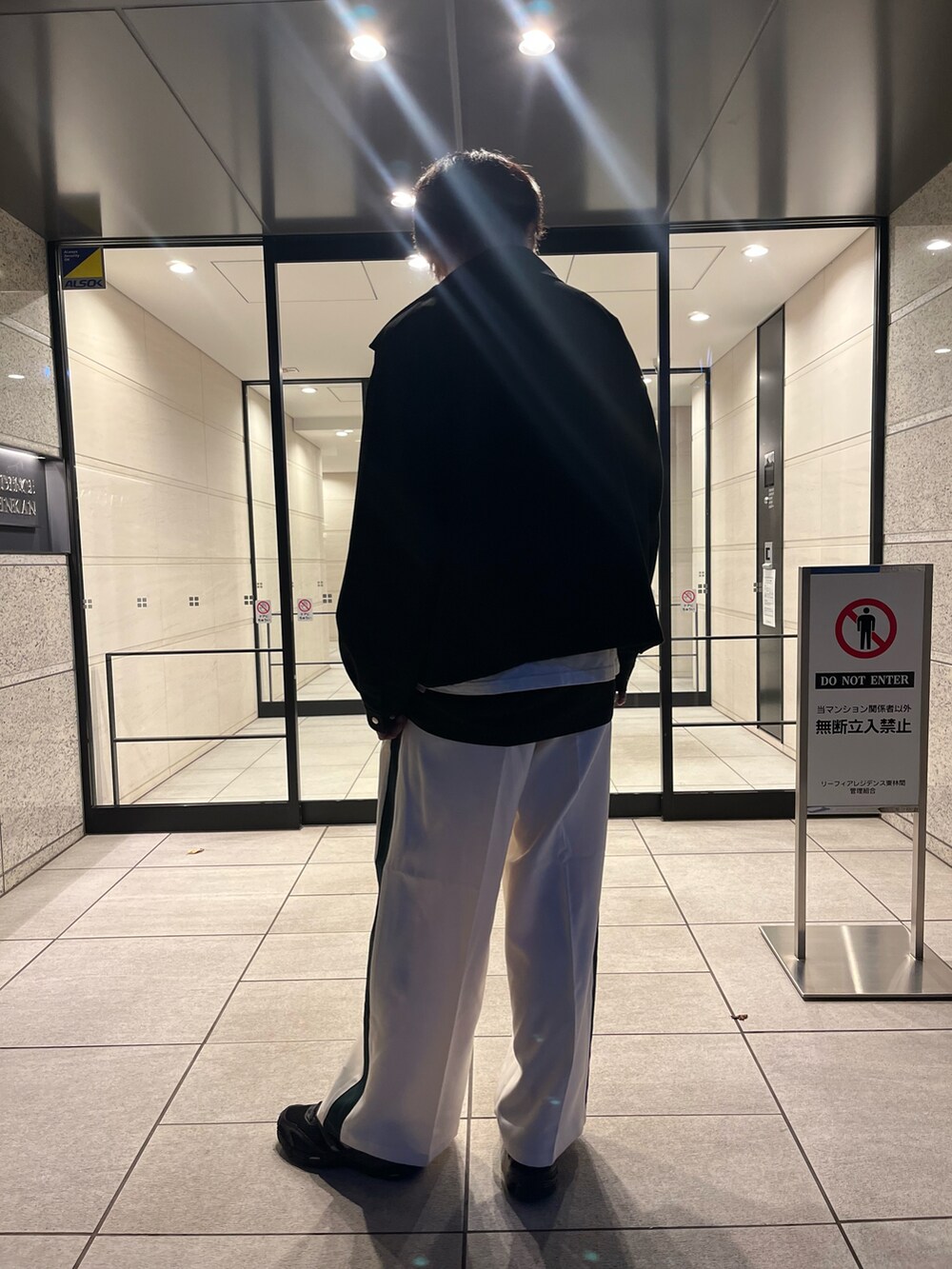 ホワイト系のスラックス、ブラック系のスニーカー、ブラック系のタンクトップを着用したメンズの秋コーディネートの3枚目の写真