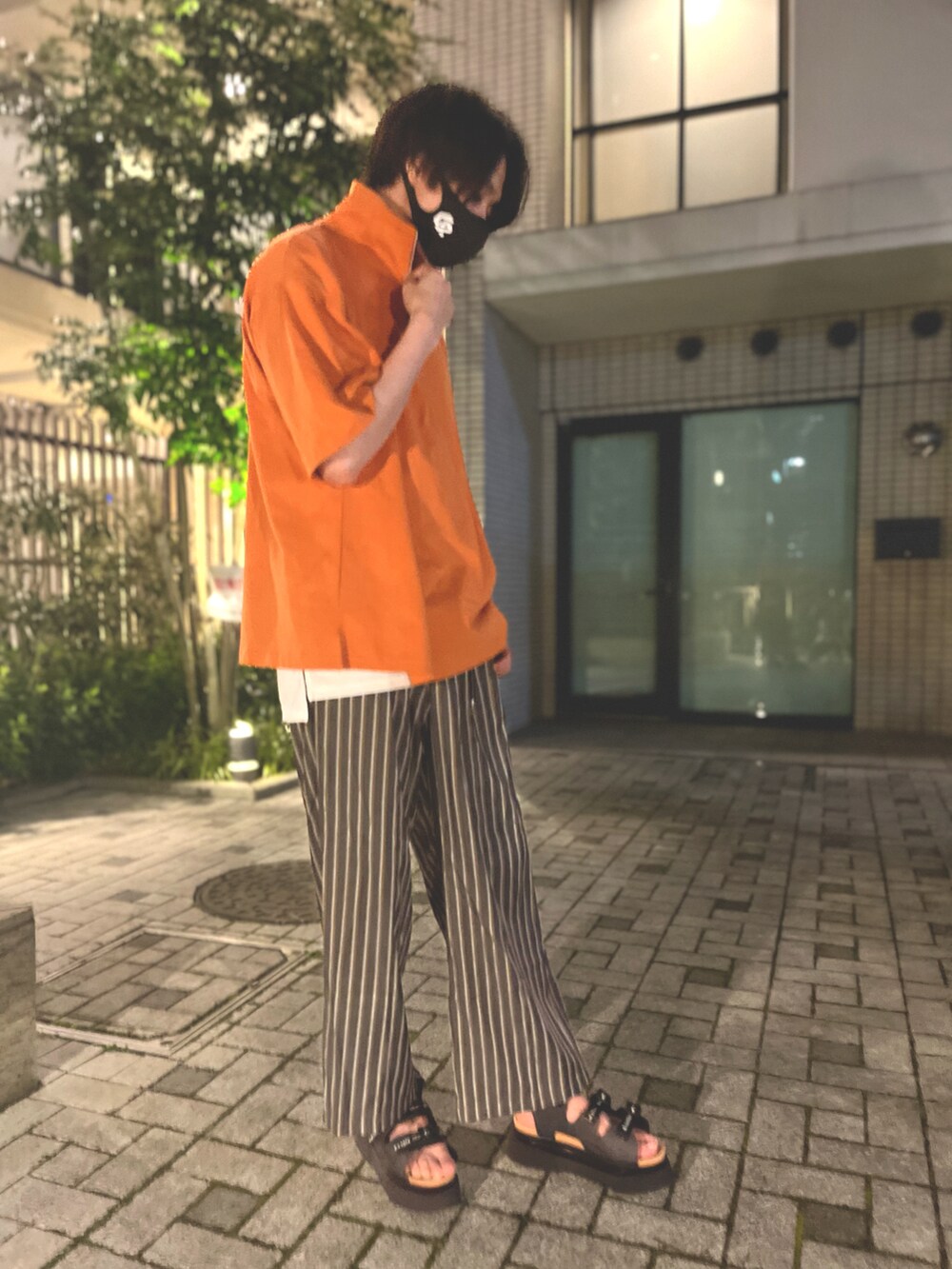 オレンジ系のTシャツ/カットソー、ブラック系のその他パンツ、ブラック系のサンダルを着用したメンズの夏コーディネートの2枚目の写真