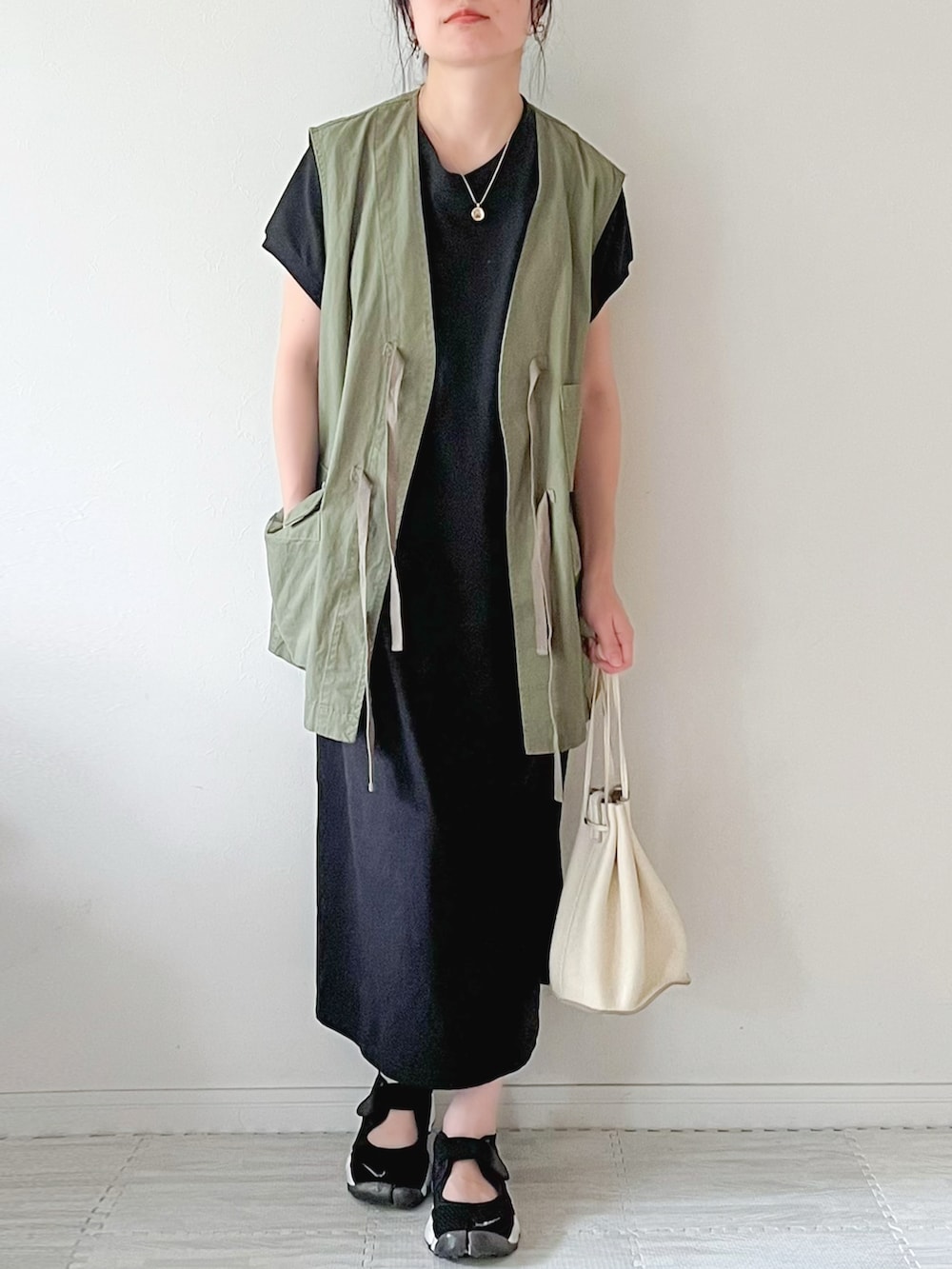 ブラック系のワンピース、グリーン系のベスト、ブラック系のスニーカーを着用したレディースの夏コーディネートの2枚目の写真