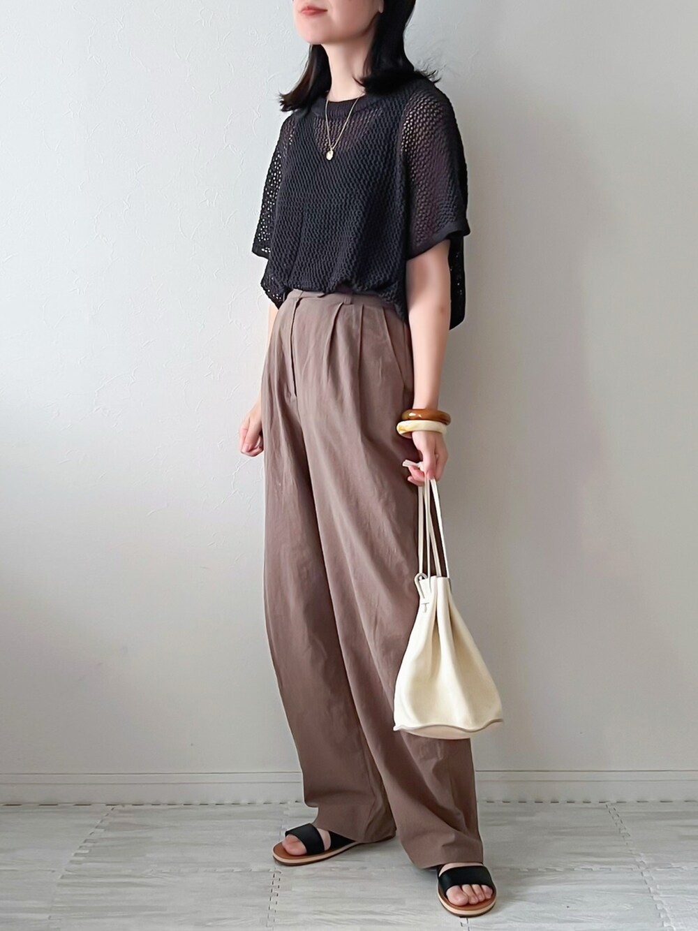 グレー系のニット/セーター、ブラウン系のスラックス、ベージュ系のショルダーバッグを着用したレディースの夏コーディネートの2枚目の写真