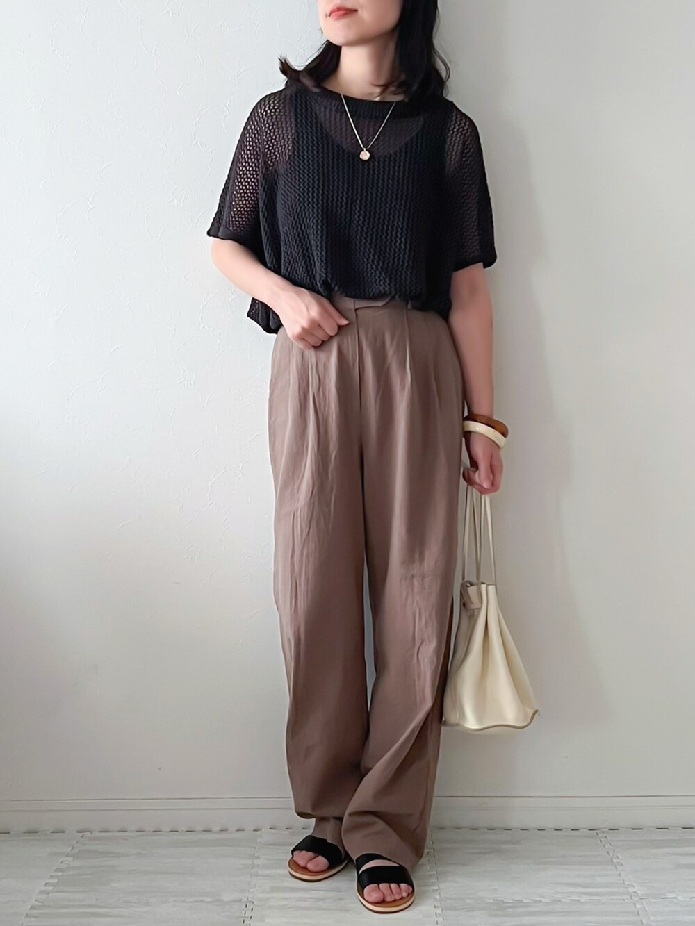 グレー系のニット/セーター、ブラウン系のスラックス、ベージュ系のショルダーバッグを着用したレディースの夏コーディネートの3枚目の写真