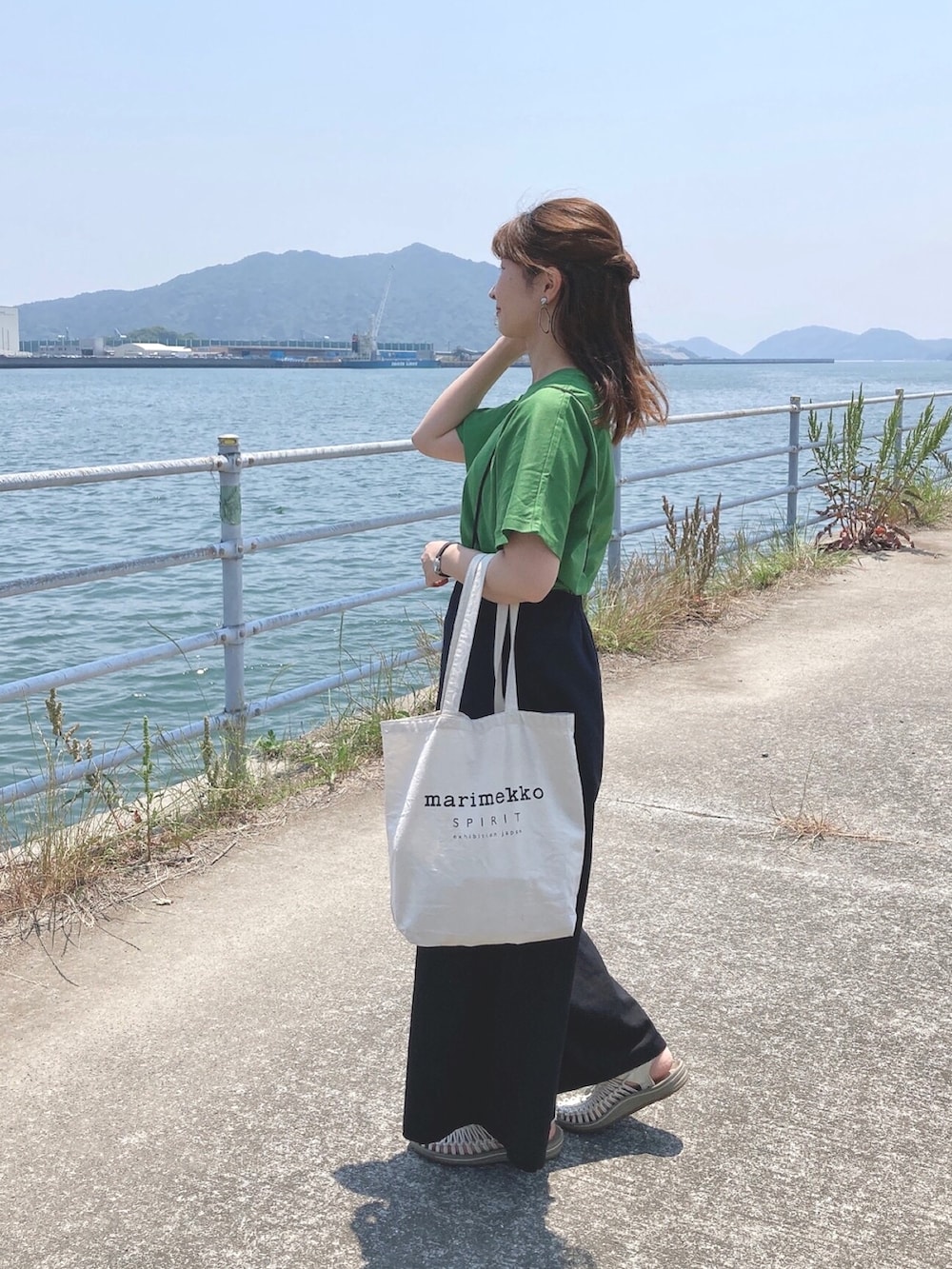 ホワイト系のトートバッグ、ベージュ系のサンダル、グリーン系のTシャツ/カットソーを着用したレディースの春コーディネートの2枚目の写真