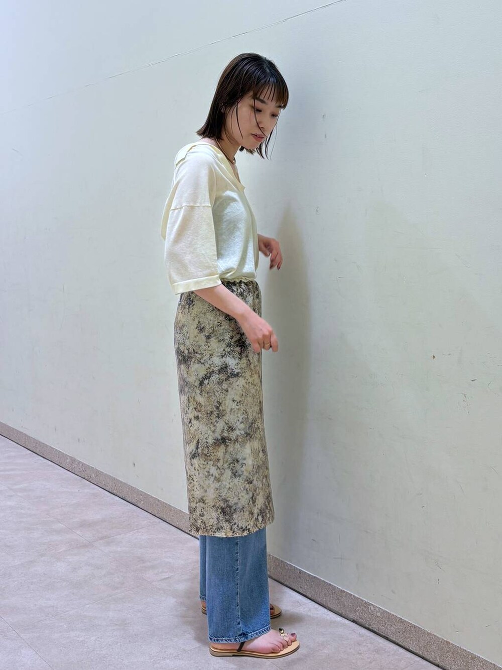 ベージュ系のスカート、イエロー系のニット/セーター、ブルー系のデニムパンツを着用したレディースの春コーディネートの2枚目の写真