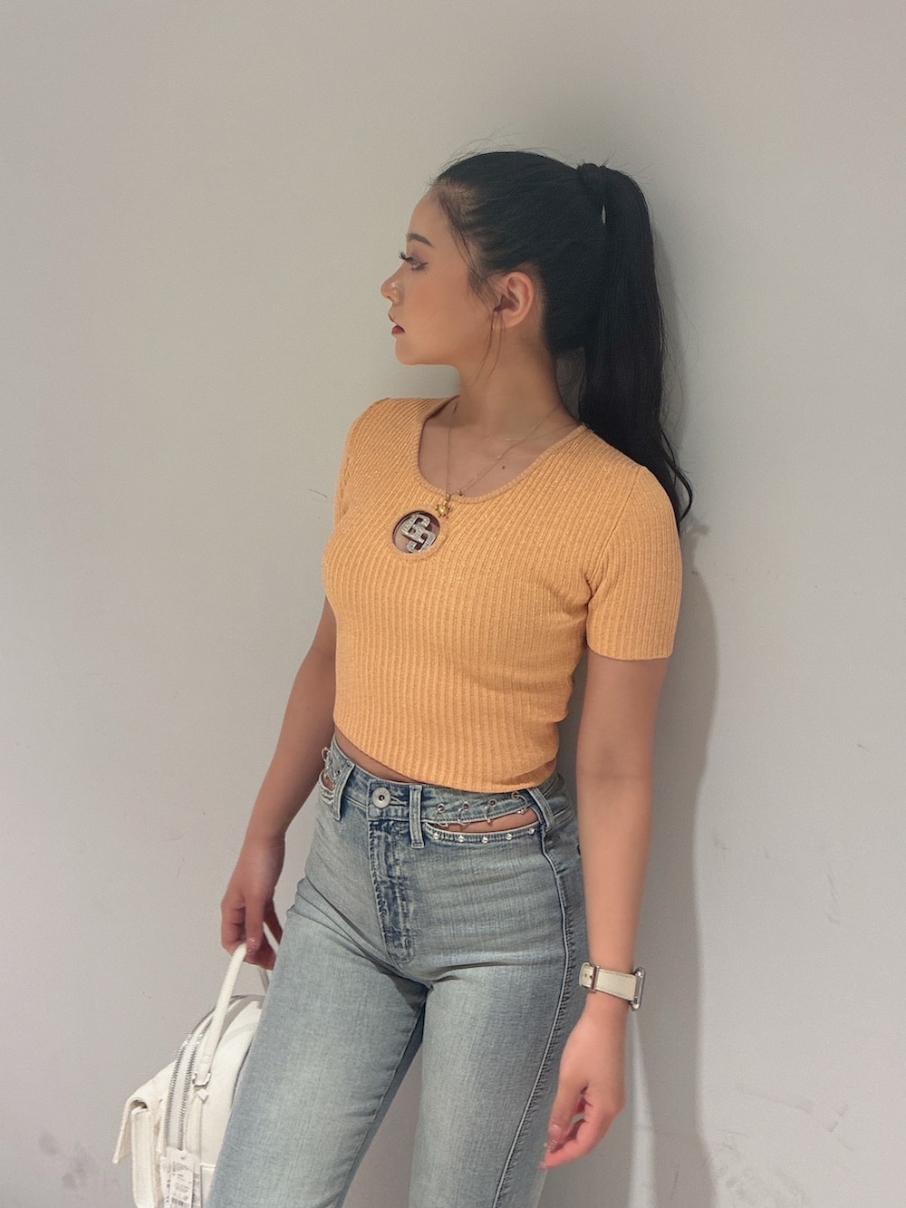 オレンジ系のニット/セーター、ブルー系のデニムパンツ、ホワイト系のバックパック/リュックを着用したレディースの春コーディネートの2枚目の写真