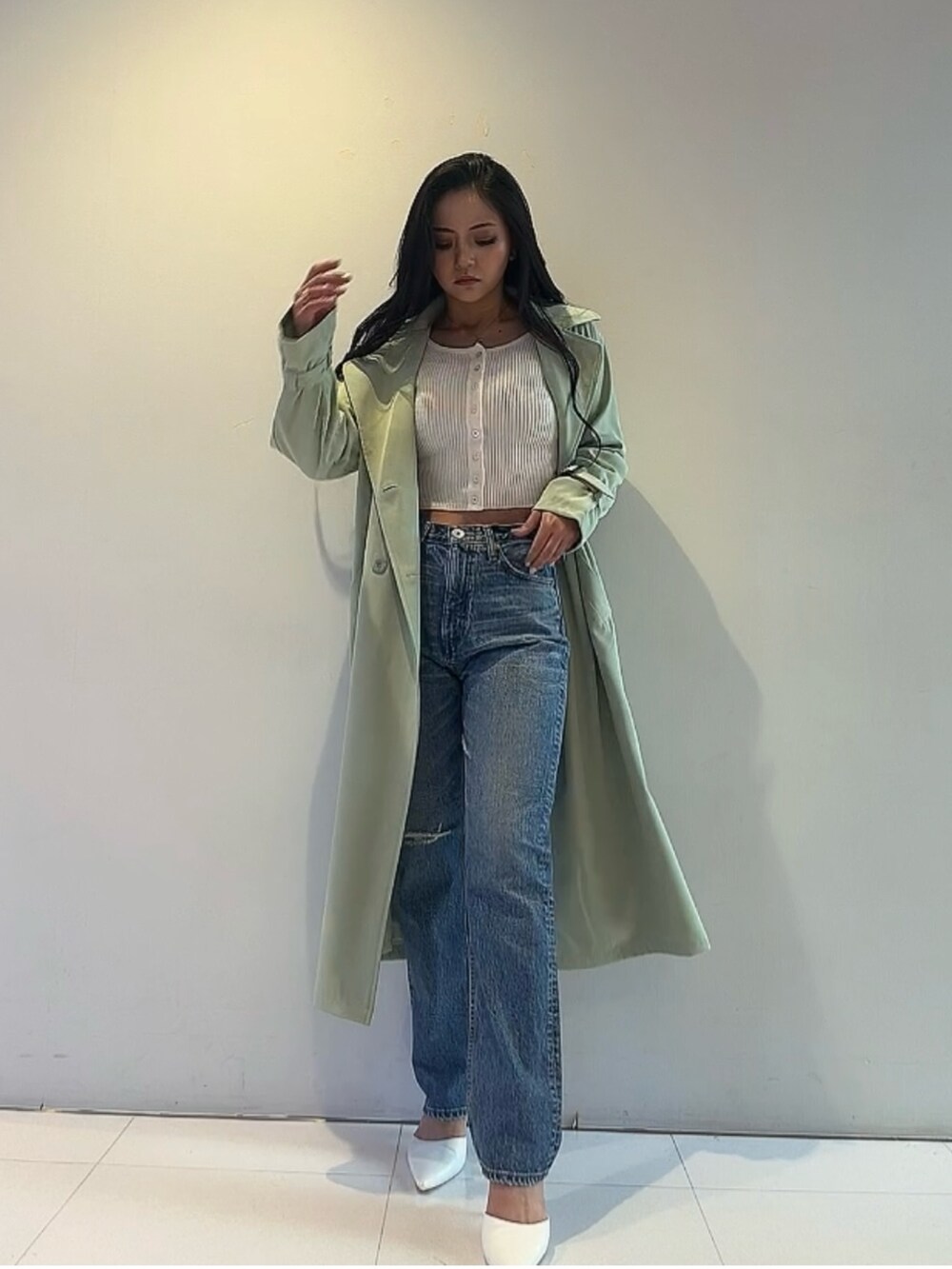 グリーン系のトレンチコート、ホワイト系のカーディガン/ボレロ、ブルー系のデニムパンツを着用したレディースの春コーディネートの2枚目の写真