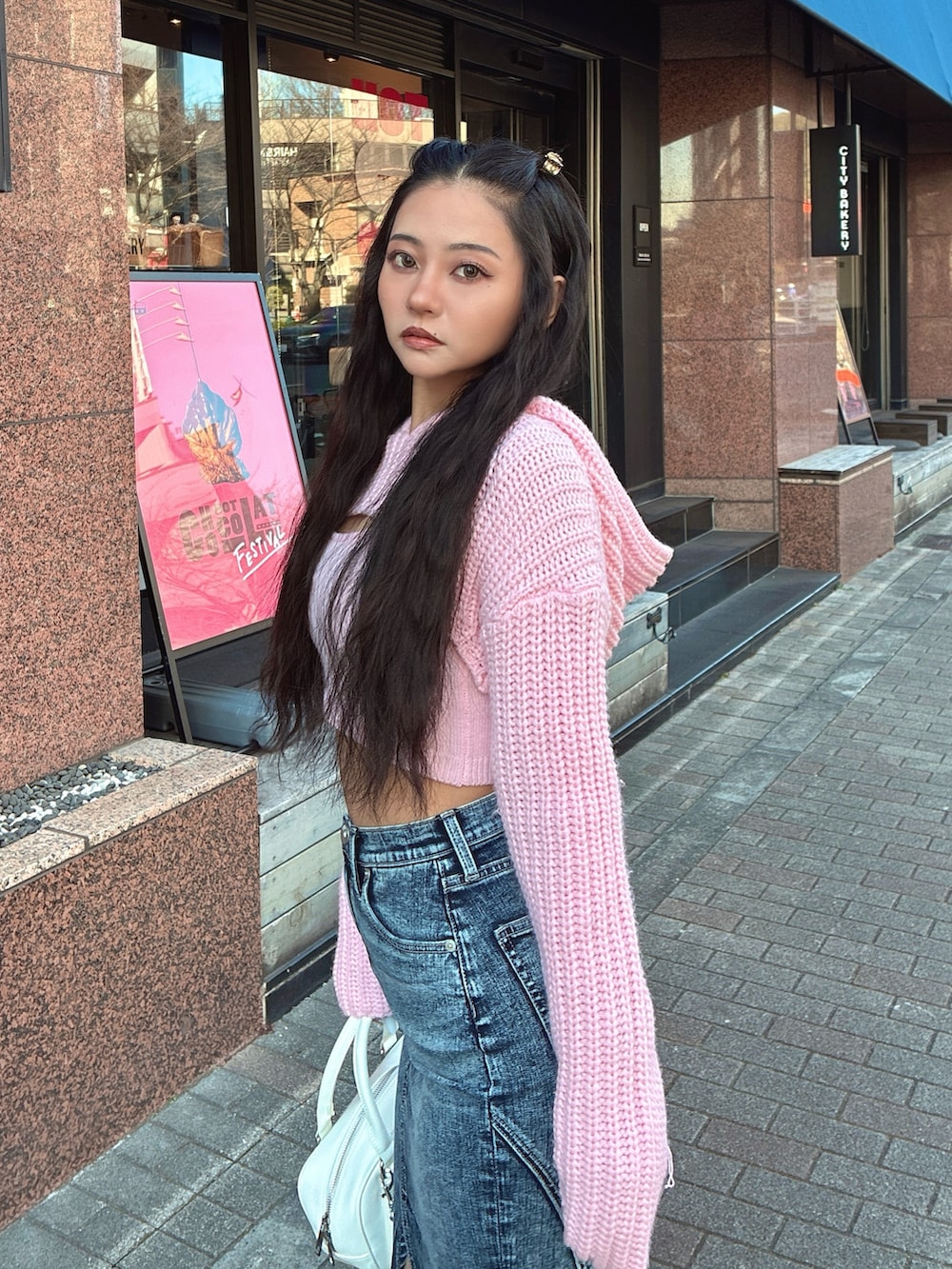 ピンク系のニット/セーター、ブルー系のデニムスカート、ホワイト系のブーツを着用したレディースの冬コーディネートの3枚目の写真