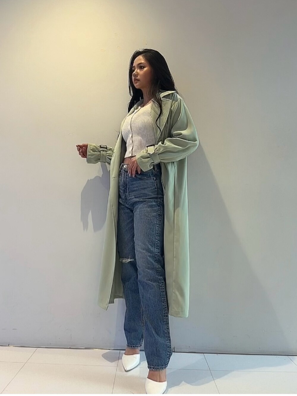グリーン系のトレンチコート、ホワイト系のカーディガン/ボレロ、ブルー系のデニムパンツを着用したレディースの春コーディネートの3枚目の写真