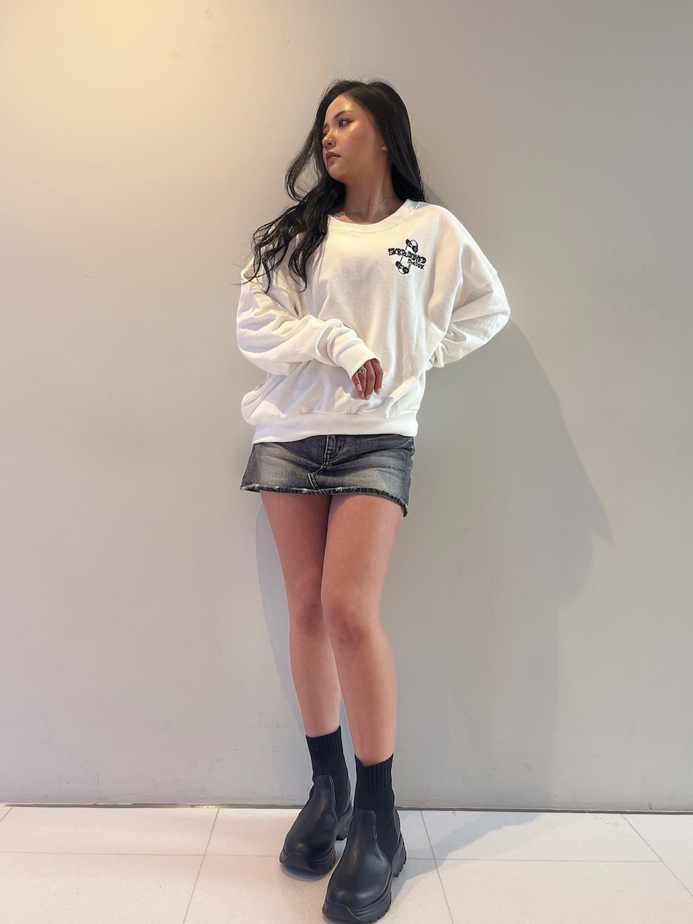 ホワイト系のスウェット、ブラック系のデニムスカート、ブラック系のブーツを着用したレディースの春コーディネートの2枚目の写真