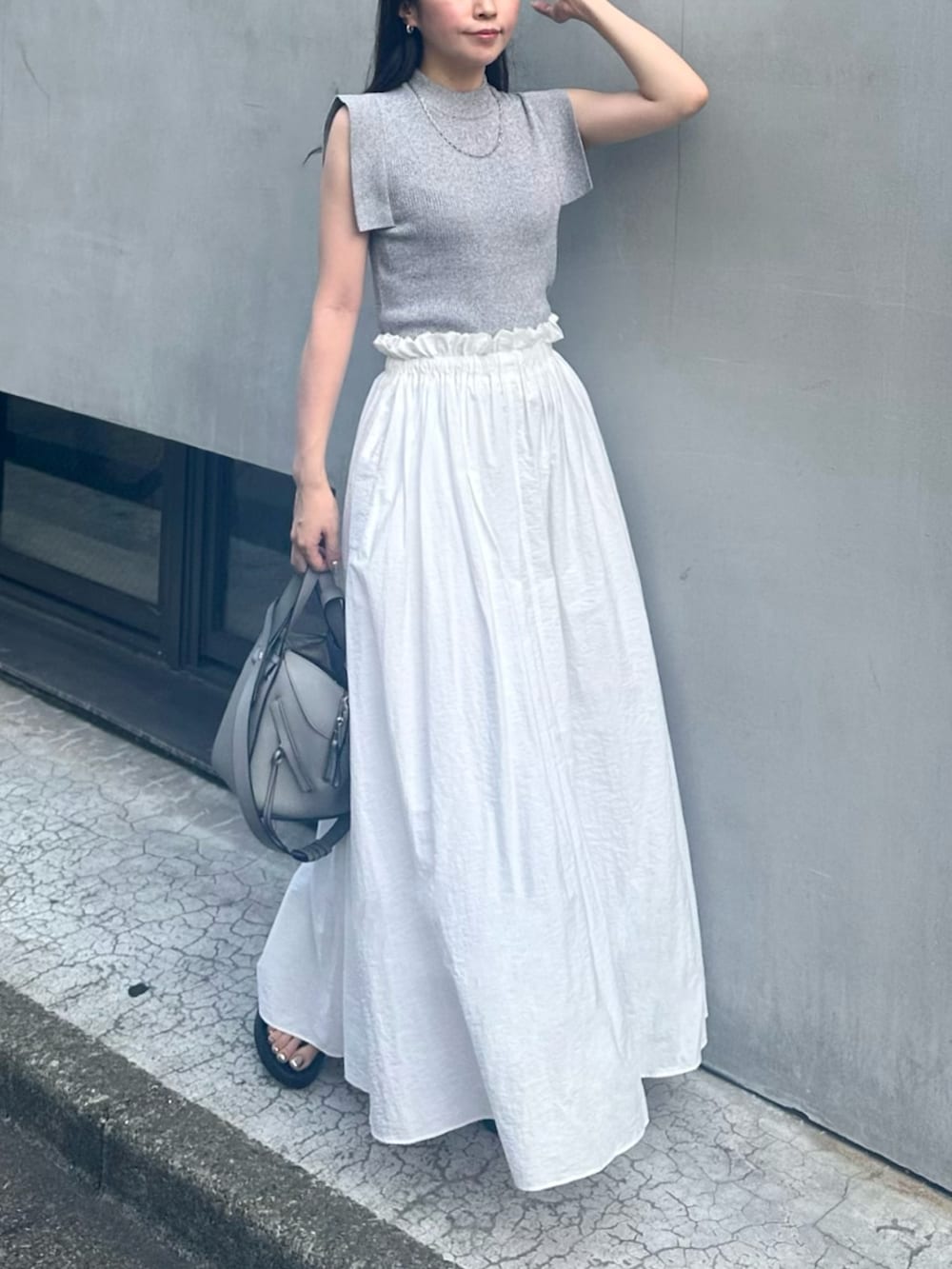 グレー系のトートバッグ、ホワイト系のスカート、グレー系のニット/セーターを着用したレディースの夏コーディネートの2枚目の写真