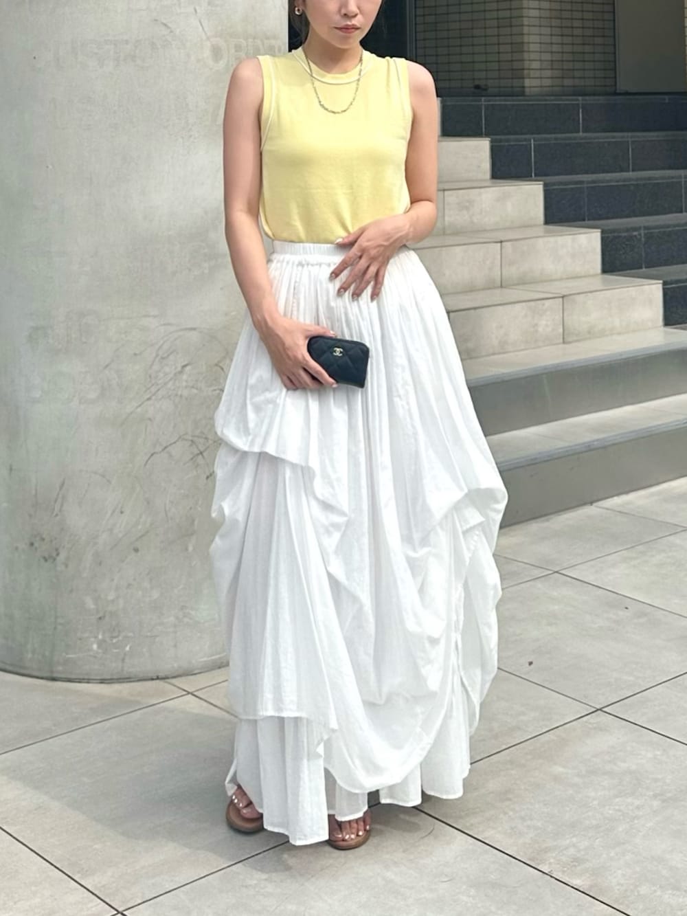 イエロー系のタンクトップ、ホワイト系のスカート、シルバー系のピアス（両耳用）を着用したレディースの夏コーディネートの2枚目の写真