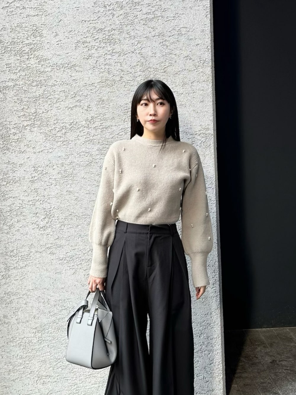 グレー系のトートバッグ、ブラック系のスラックス、ベージュ系のニット/セーターを着用したレディースの冬コーディネートの3枚目の写真