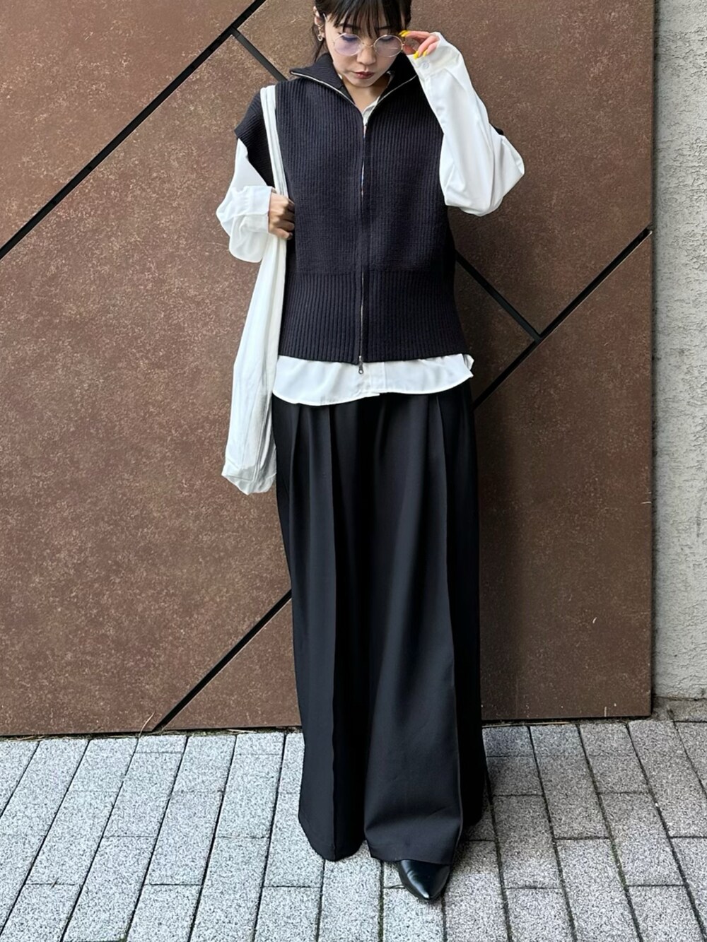 ブラック系のスラックス、ホワイト系のシャツ/ブラウス、ブラック系のニット/セーターを着用したレディースの春コーディネートの2枚目の写真