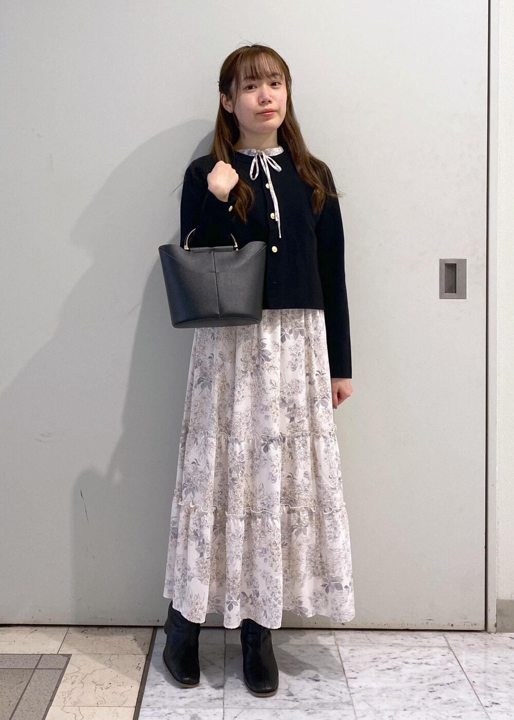 ホワイト系のワンピース、ブラック系のカーディガン/ボレロ、ブラック系のブーツを着用したレディースの冬コーディネートの2枚目の写真