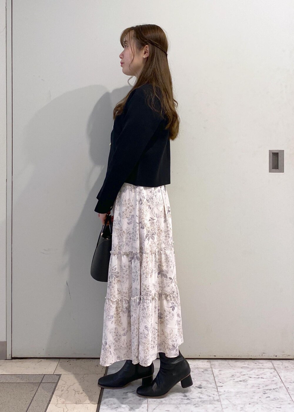 ホワイト系のワンピース、ブラック系のカーディガン/ボレロ、ブラック系のブーツを着用したレディースの冬コーディネートの3枚目の写真