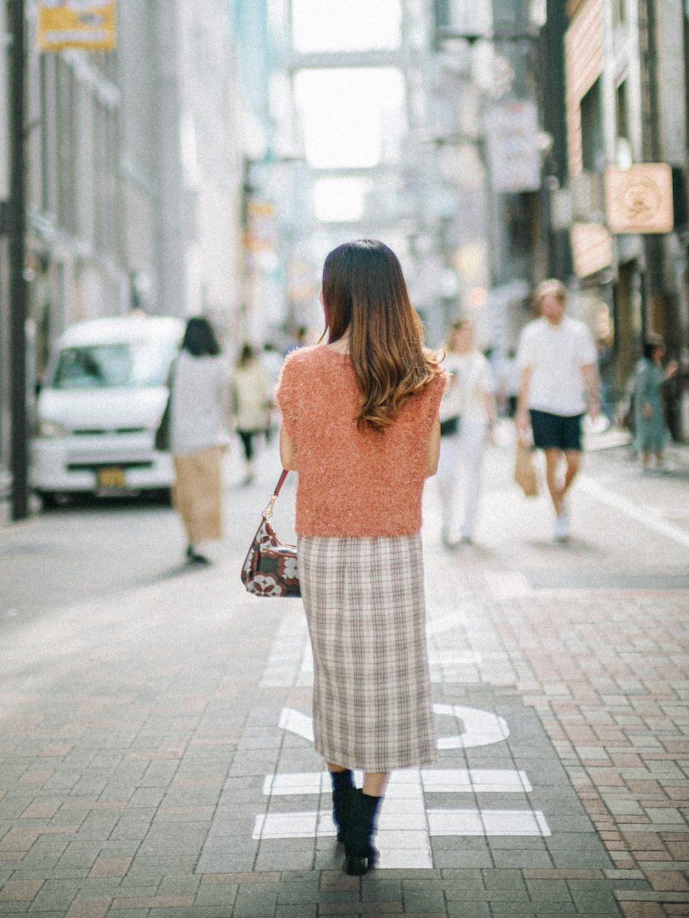 オレンジ系のニット/セーター、ブラウン系のショルダーバッグ、ホワイト系のスカートを着用したレディースの秋コーディネートの4枚目の写真