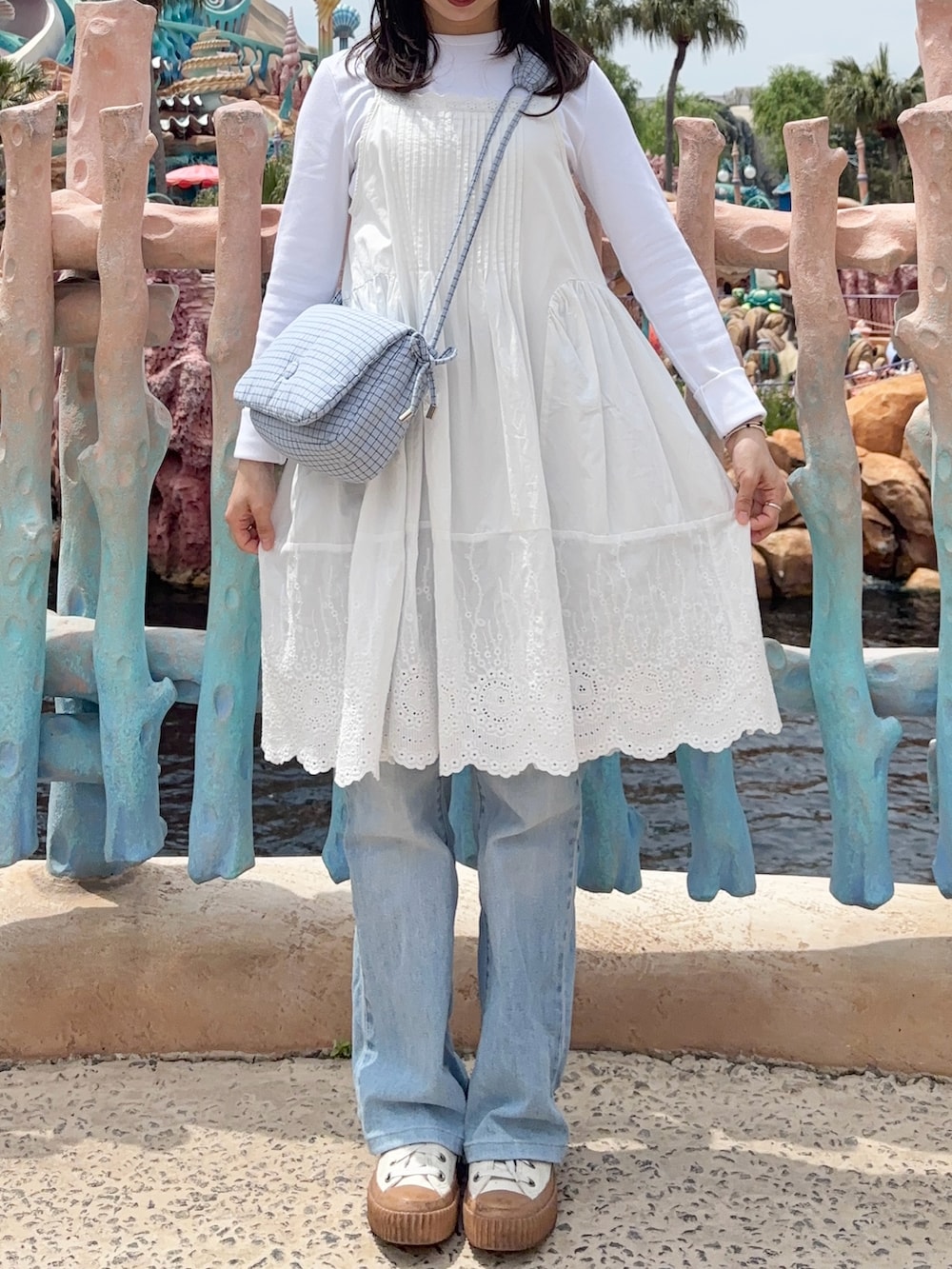 ブルー系のショルダーバッグ、ホワイト系のワンピース、ブルー系のデニムパンツを着用したレディースの春コーディネートの2枚目の写真