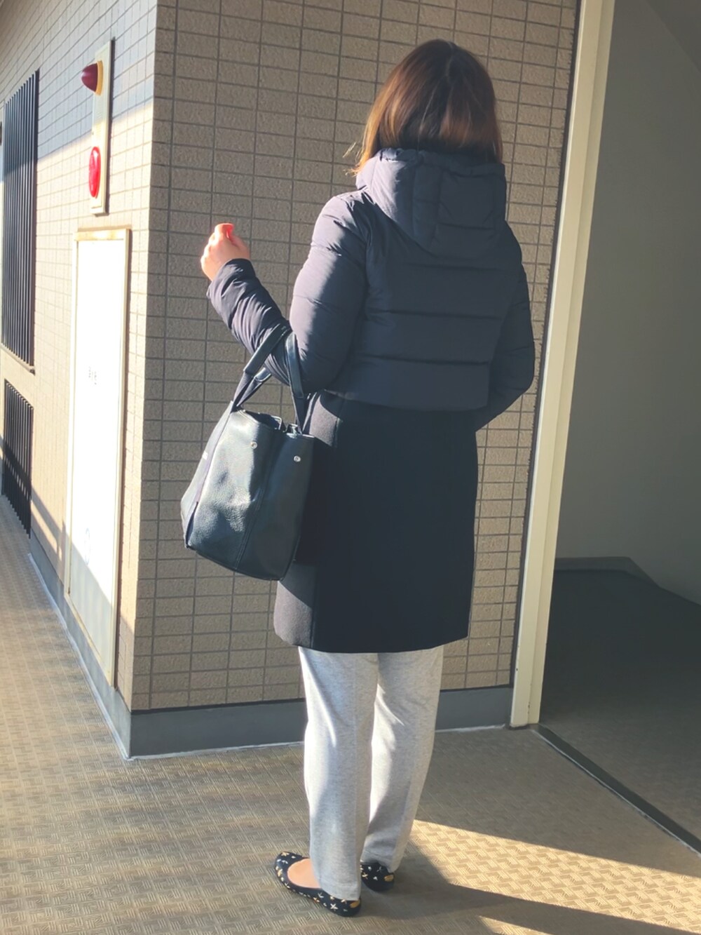 ブラック系のダウンジャケット/コート、ブラック系のトートバッグ、グレー系のスラックスを着用したレディースの春コーディネートの2枚目の写真