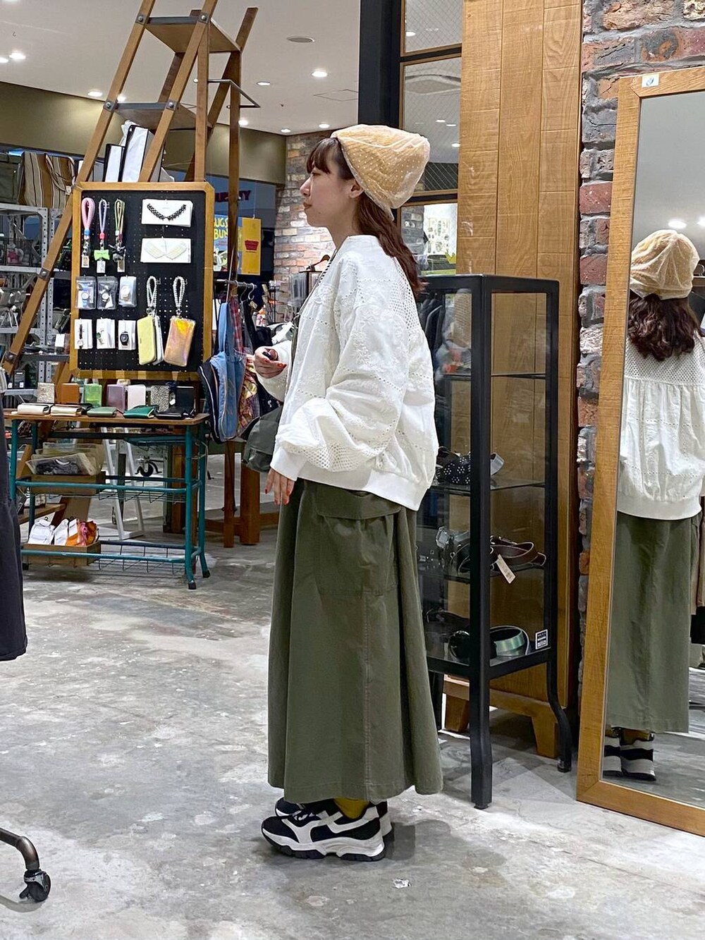 ホワイト系のTシャツ/カットソー、グリーン系のジャンパースカート、ブラック系のスニーカーを着用したレディースの春コーディネートの2枚目の写真