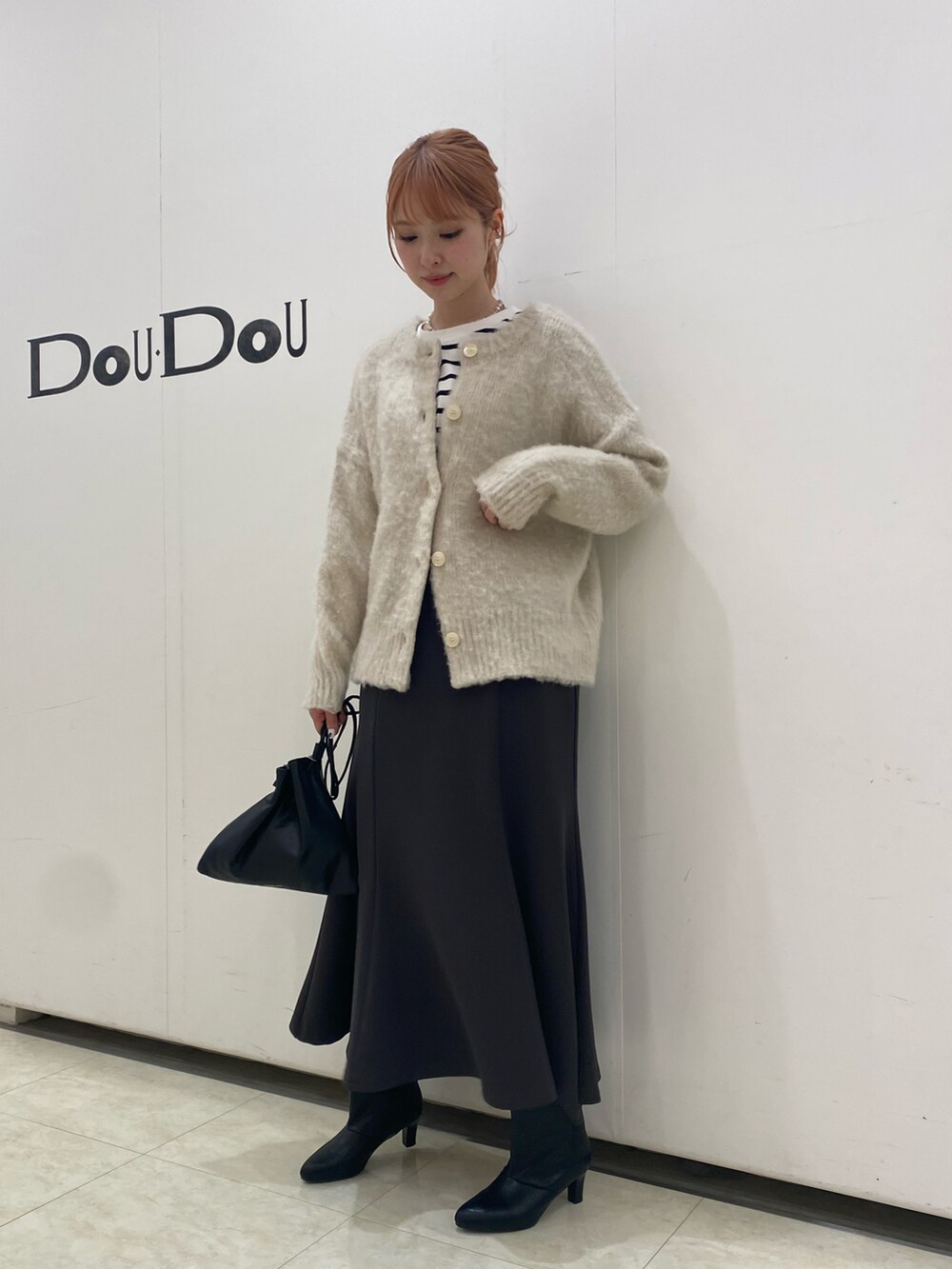 ベージュ系のニット/セーター、グレー系のスカート、ブラック系のブーツを着用したレディースの冬コーディネートの2枚目の写真
