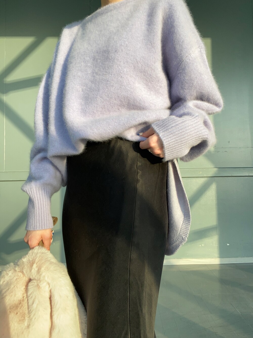 パープル系のニット/セーター、ベージュ系のハンドバッグ、ブラック系のスカートを着用したレディースの冬コーディネートの4枚目の写真