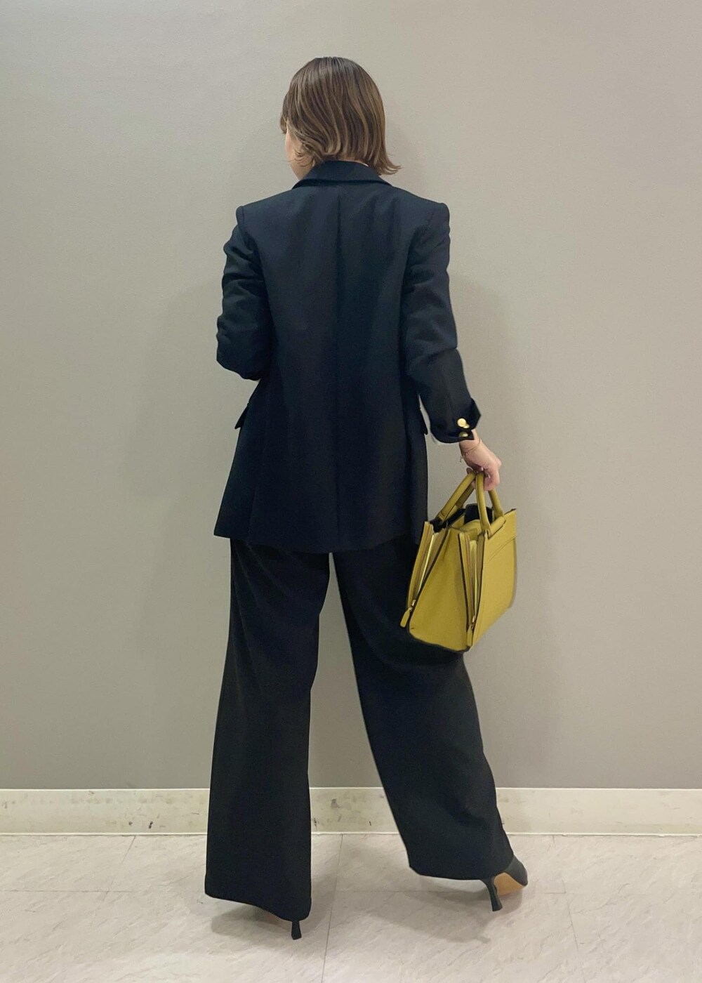 ブルー系のテーラードジャケット、イエロー系のハンドバッグ、ブラック系のブーツを着用したレディースの秋コーディネートの3枚目の写真