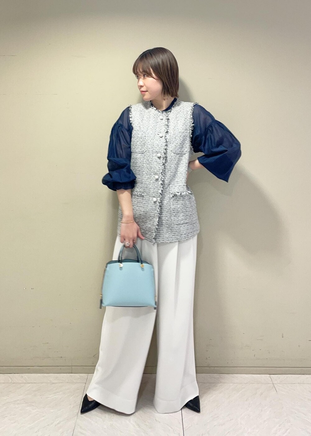 ブラック系のパンプス、ブルー系のハンドバッグ、ブラック系のベストを着用したレディースの冬コーディネートの2枚目の写真