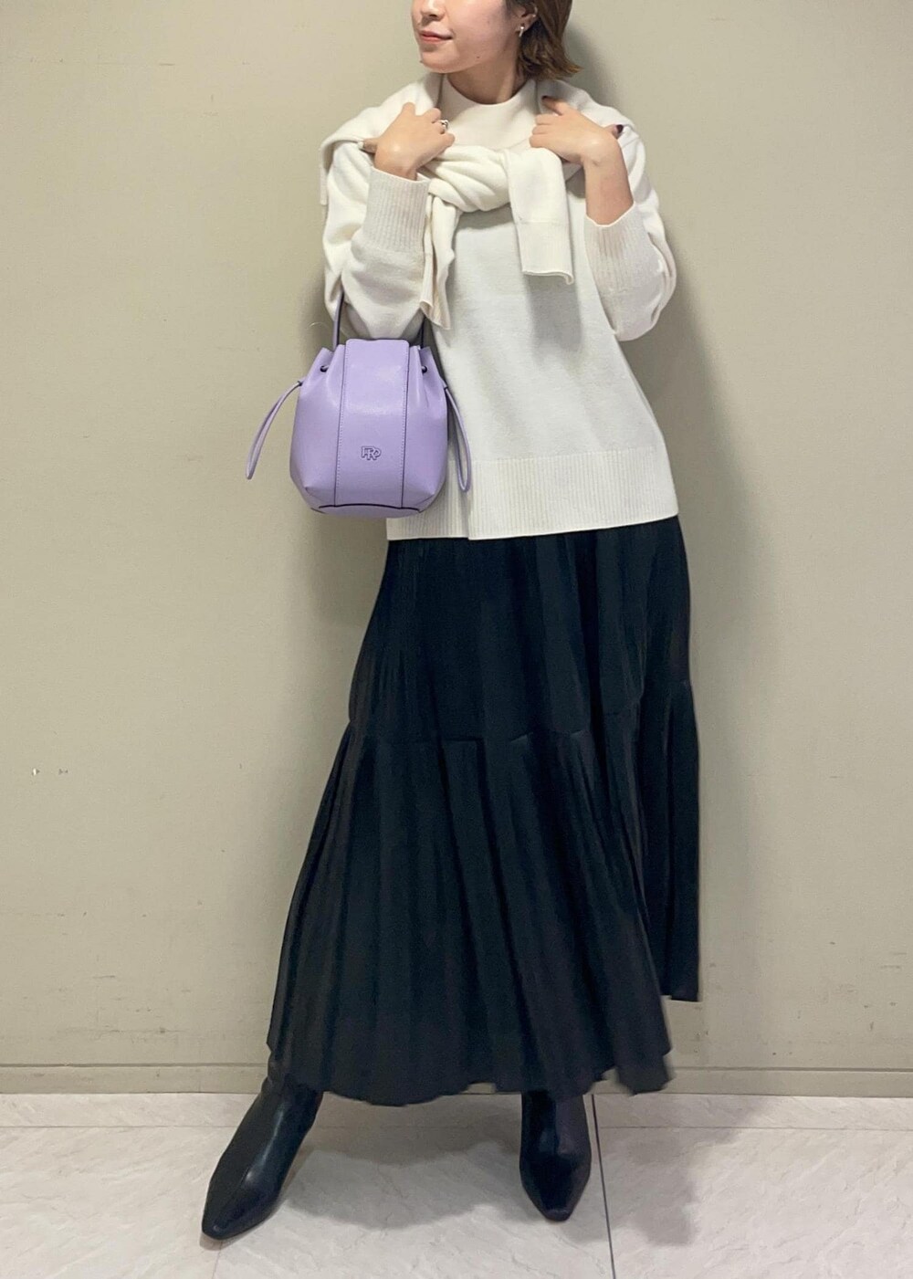パープル系のハンドバッグ、ブラック系のブーツ、ブラック系のスカートを着用したレディースの秋コーディネートの4枚目の写真