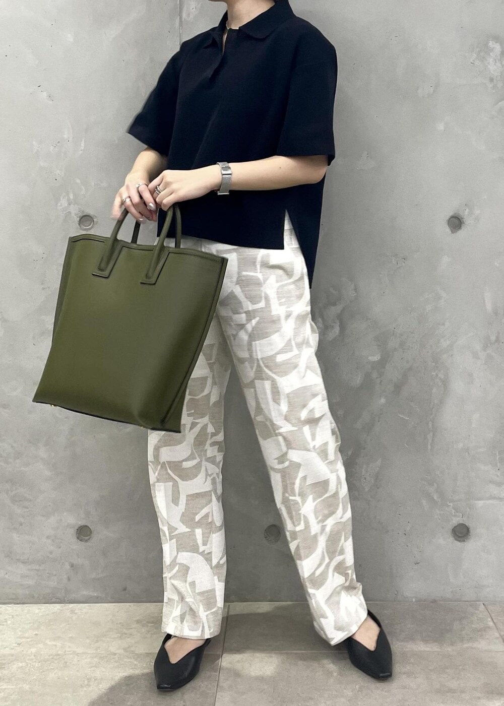 グリーン系のトートバッグ、ブラック系のパンプス、ブルー系のニット/セーターを着用したレディースの春コーディネートの3枚目の写真