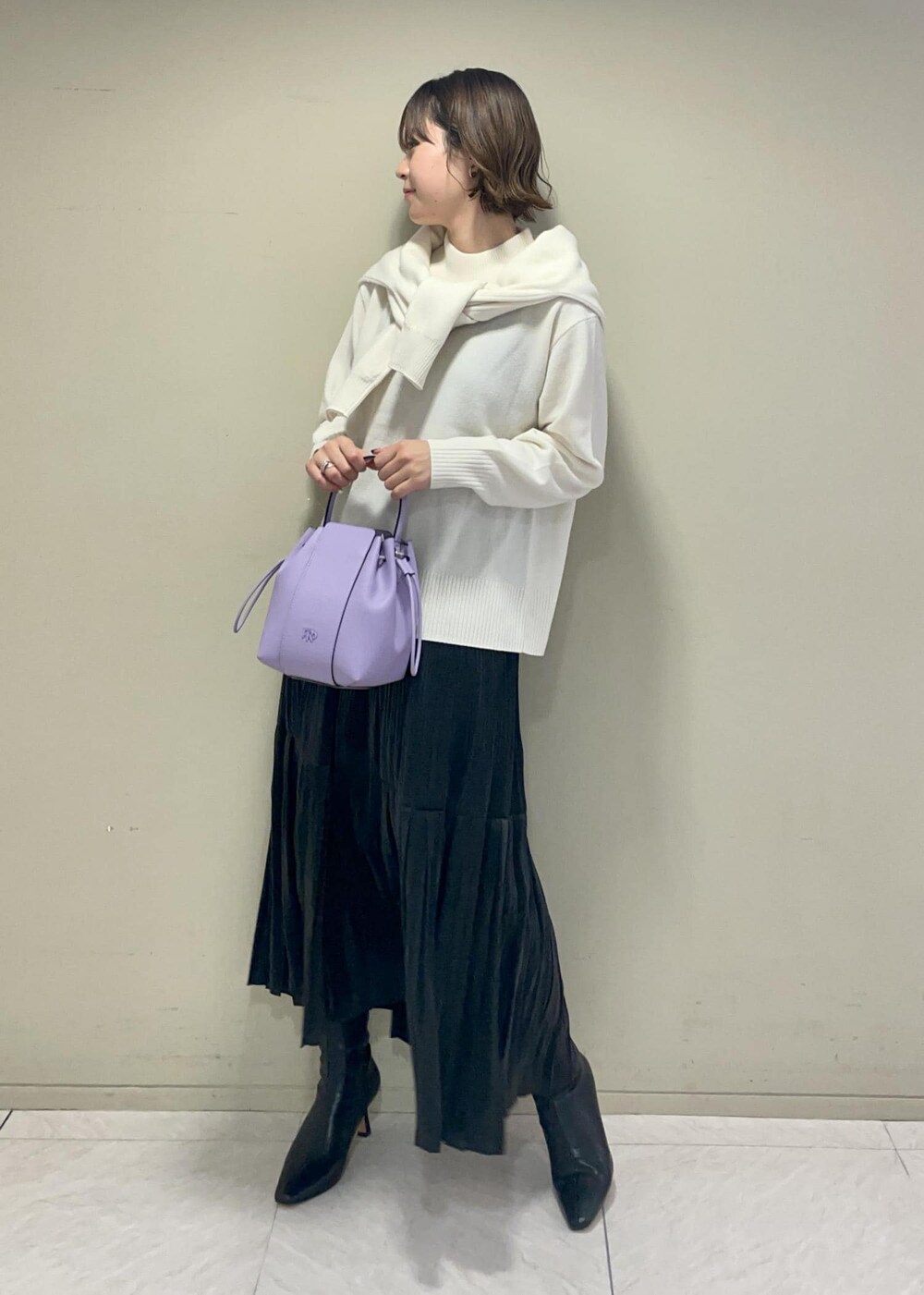 パープル系のハンドバッグ、ブラック系のブーツ、ブラック系のスカートを着用したレディースの秋コーディネートの2枚目の写真