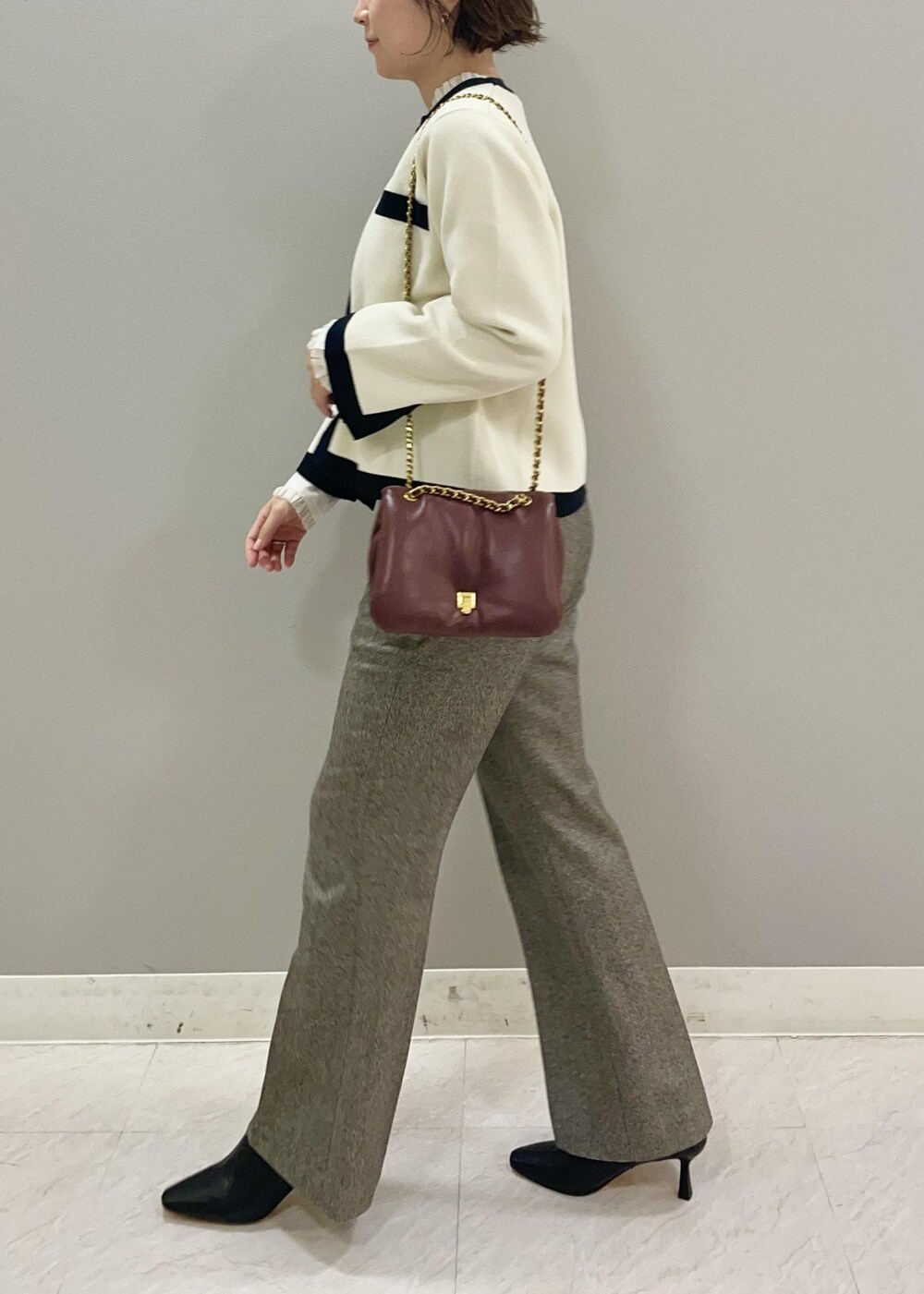 レッド系のハンドバッグ、ホワイト系のカーディガン/ボレロ、ブラック系のブーツを着用したレディースの秋コーディネートの3枚目の写真