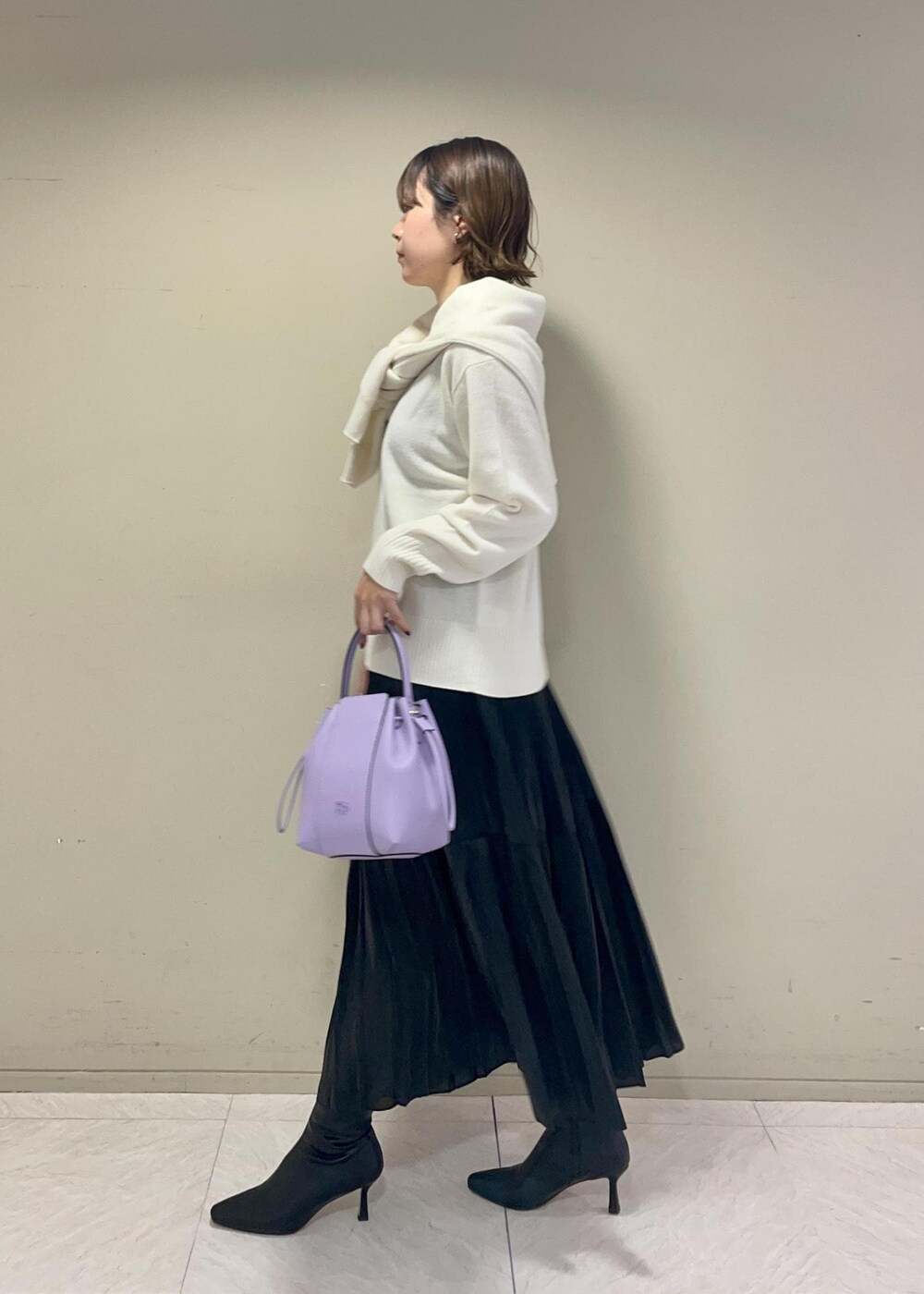 パープル系のハンドバッグ、ブラック系のブーツ、ブラック系のスカートを着用したレディースの秋コーディネートの3枚目の写真