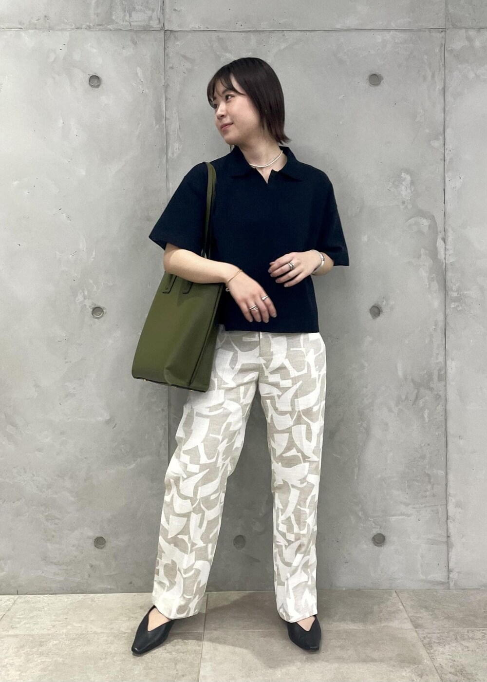 グリーン系のトートバッグ、ブラック系のパンプス、ブルー系のニット/セーターを着用したレディースの春コーディネートの2枚目の写真