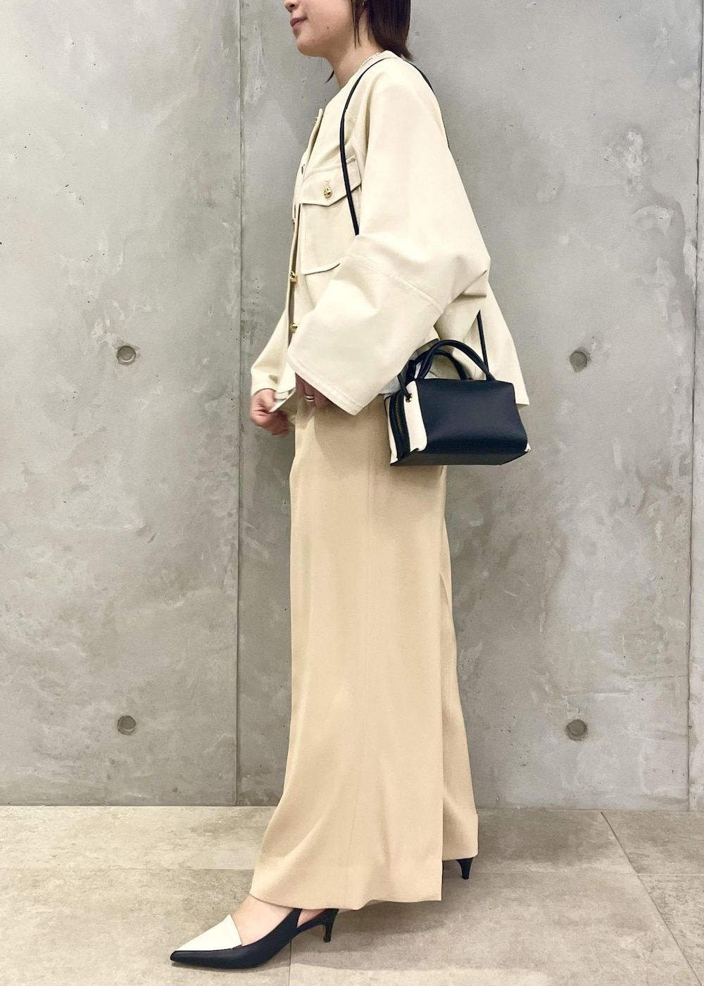 ブラック系のパンプス、ホワイト系のブルゾン、ブラック系のショルダーバッグを着用したレディースの春コーディネートの2枚目の写真