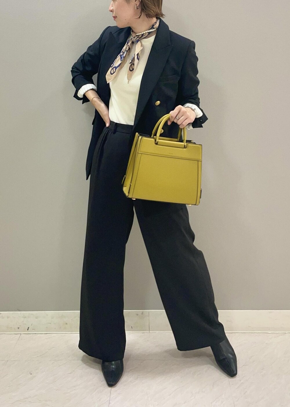 ブルー系のテーラードジャケット、イエロー系のハンドバッグ、ブラック系のブーツを着用したレディースの秋コーディネートの4枚目の写真