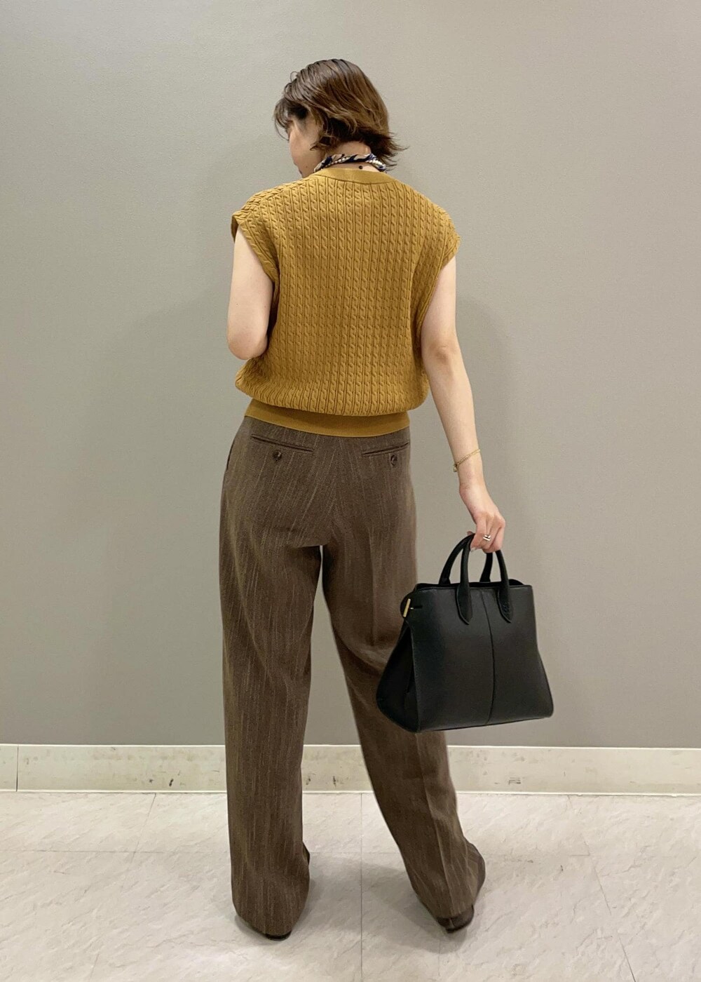 イエロー系のベスト、ブラック系のトートバッグ、ブラウン系のその他パンツを着用したレディースの夏コーディネートの2枚目の写真