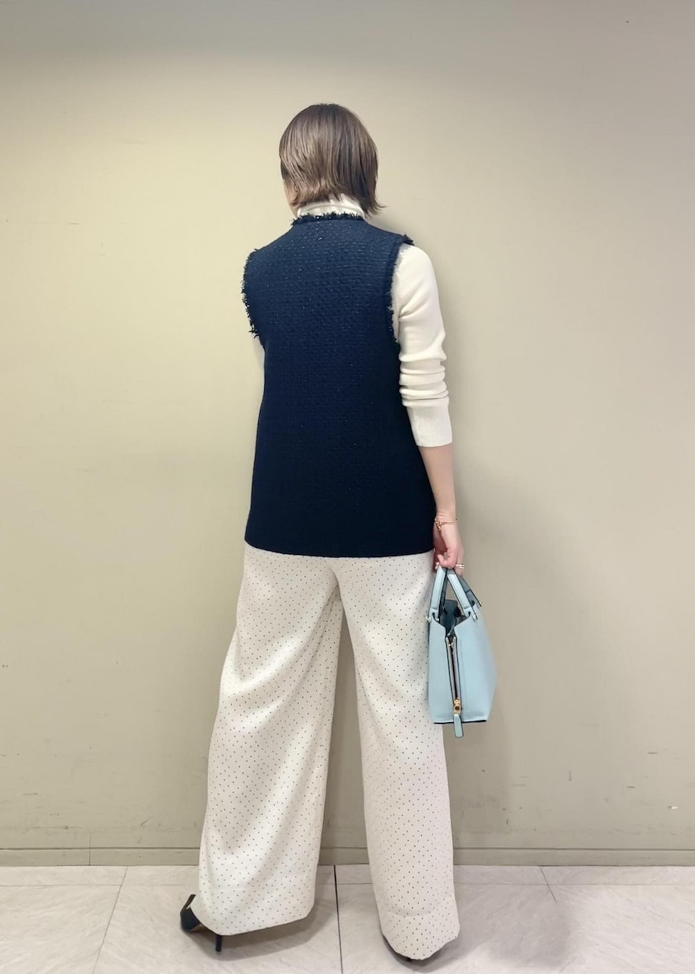 ブラック系のパンプス、ブルー系のハンドバッグ、ホワイト系のニット/セーターを着用したレディースの冬コーディネートの3枚目の写真