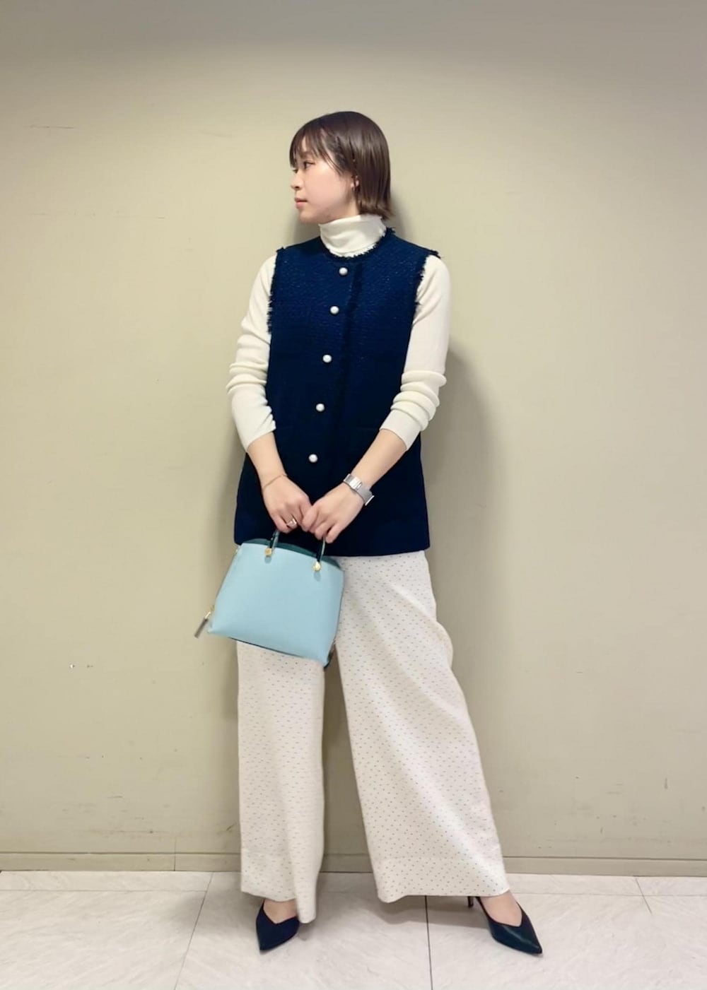 ブラック系のパンプス、ブルー系のハンドバッグ、ホワイト系のニット/セーターを着用したレディースの冬コーディネートの2枚目の写真