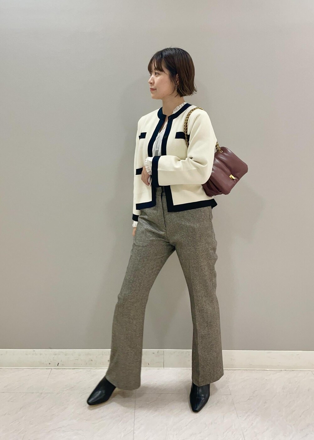 レッド系のハンドバッグ、ホワイト系のカーディガン/ボレロ、ブラック系のブーツを着用したレディースの秋コーディネートの2枚目の写真